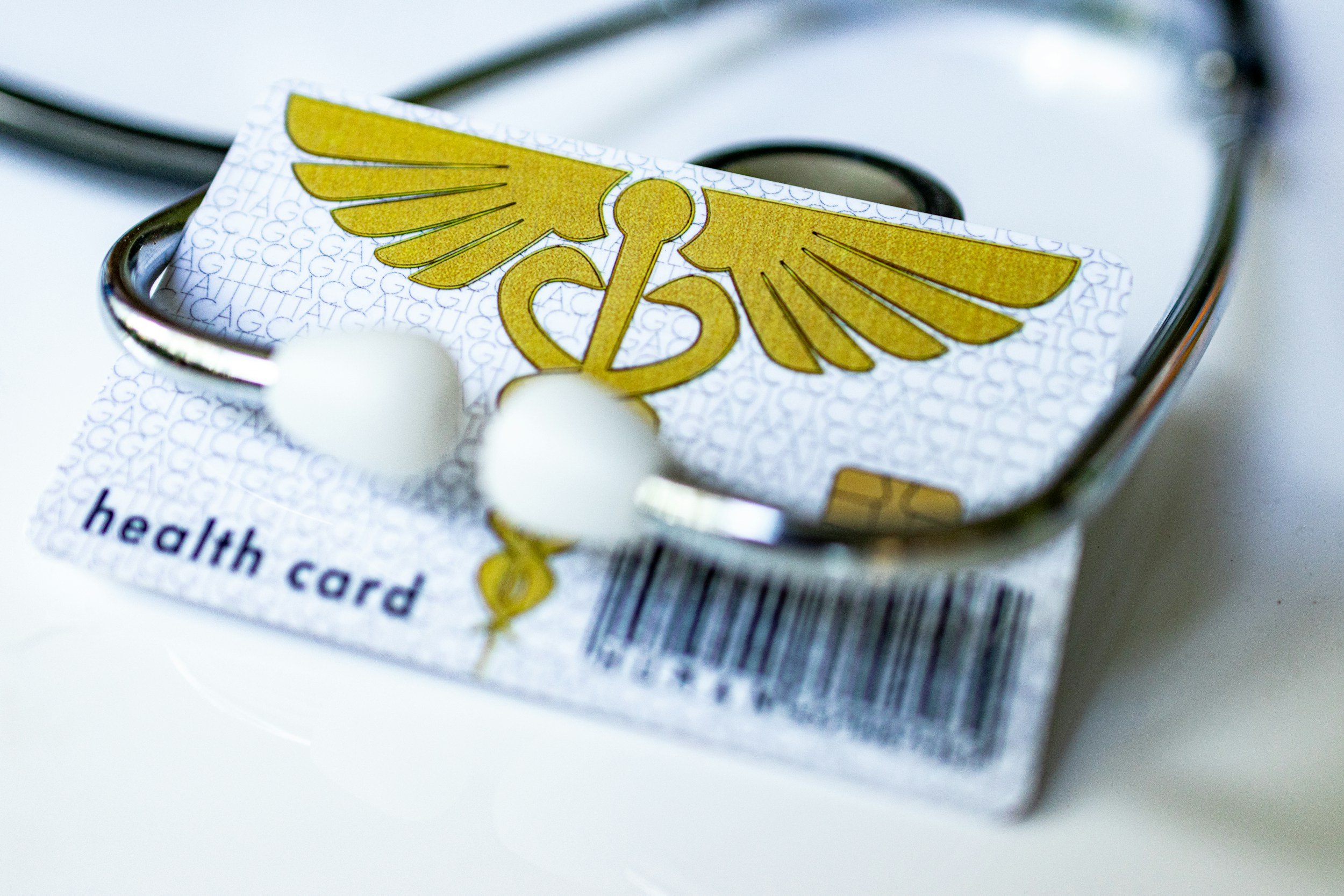 Close-up of a health card with a caduceus symbol on top, partially inside a clear plastic holder on a white surface.