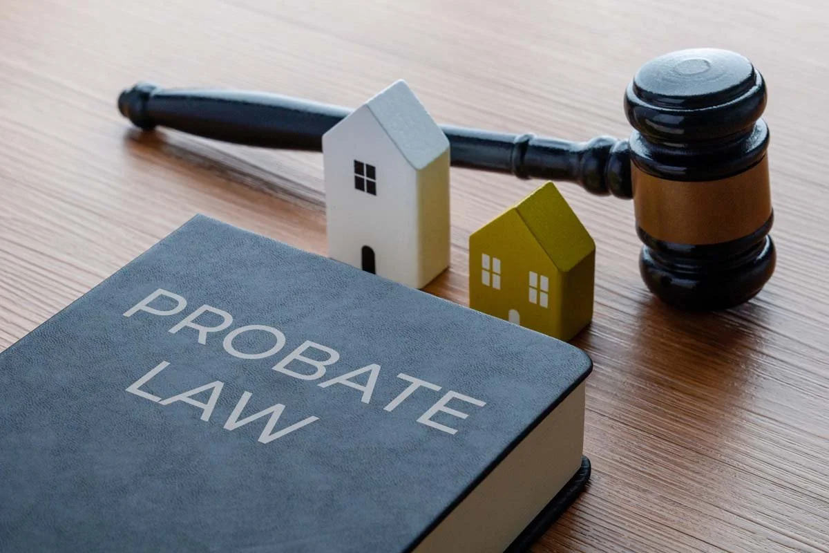 A legal gavel, a book titled 'Probate Law,' and two small houses model on a wooden surface.