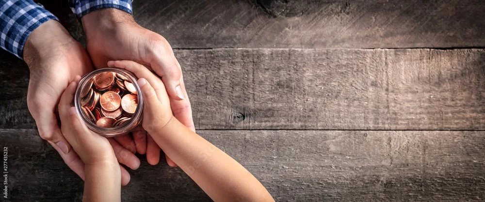 Hands holding a jar of pennies over a wooden surface.