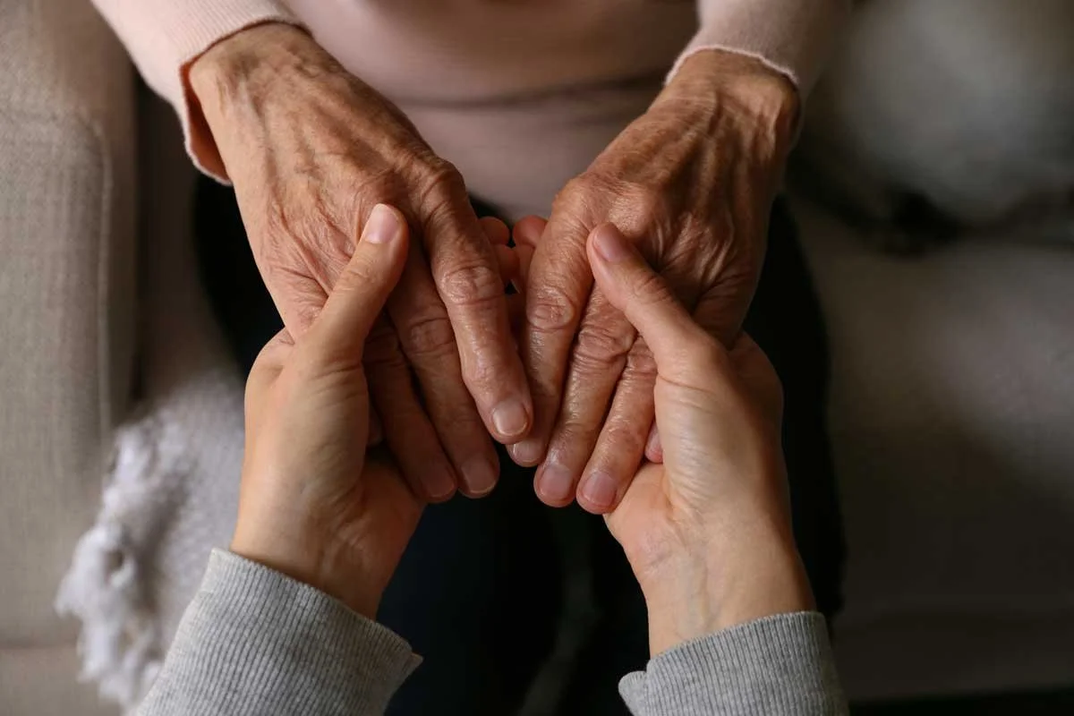 A young person holding hands with an elderly person, showing tenderness and connection.