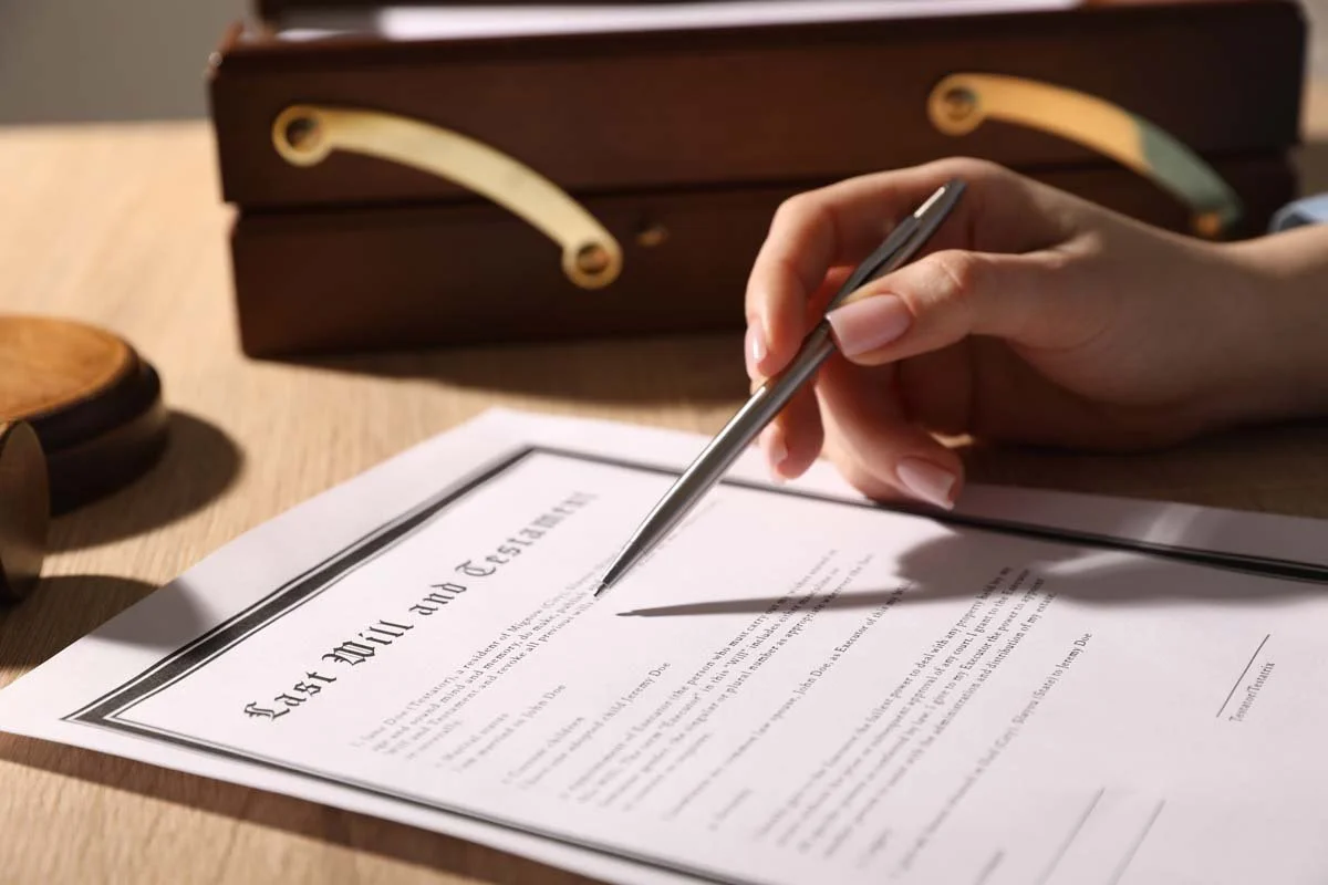 A person signing a legal document titled "Jack and Jill" with a silver pen on a wooden desk.