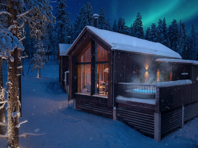Villa at night with the aurora borealis above and a steaming hot tub on the terrace