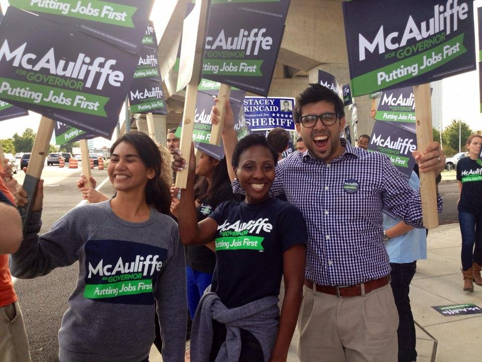 Group of people holding campaign signs that read "McAuliffe for Governor" and "Putting Jobs First," smiling at a political rally.