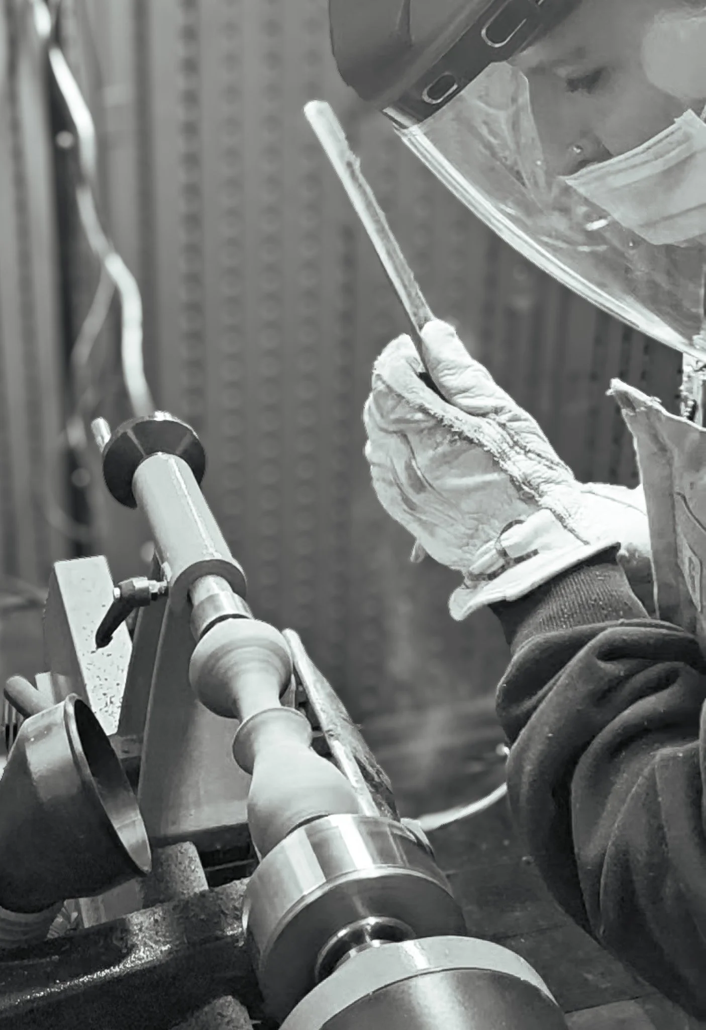 A person wearing PPE is working on a wood lathe, possibly in a workshop, with tools around.