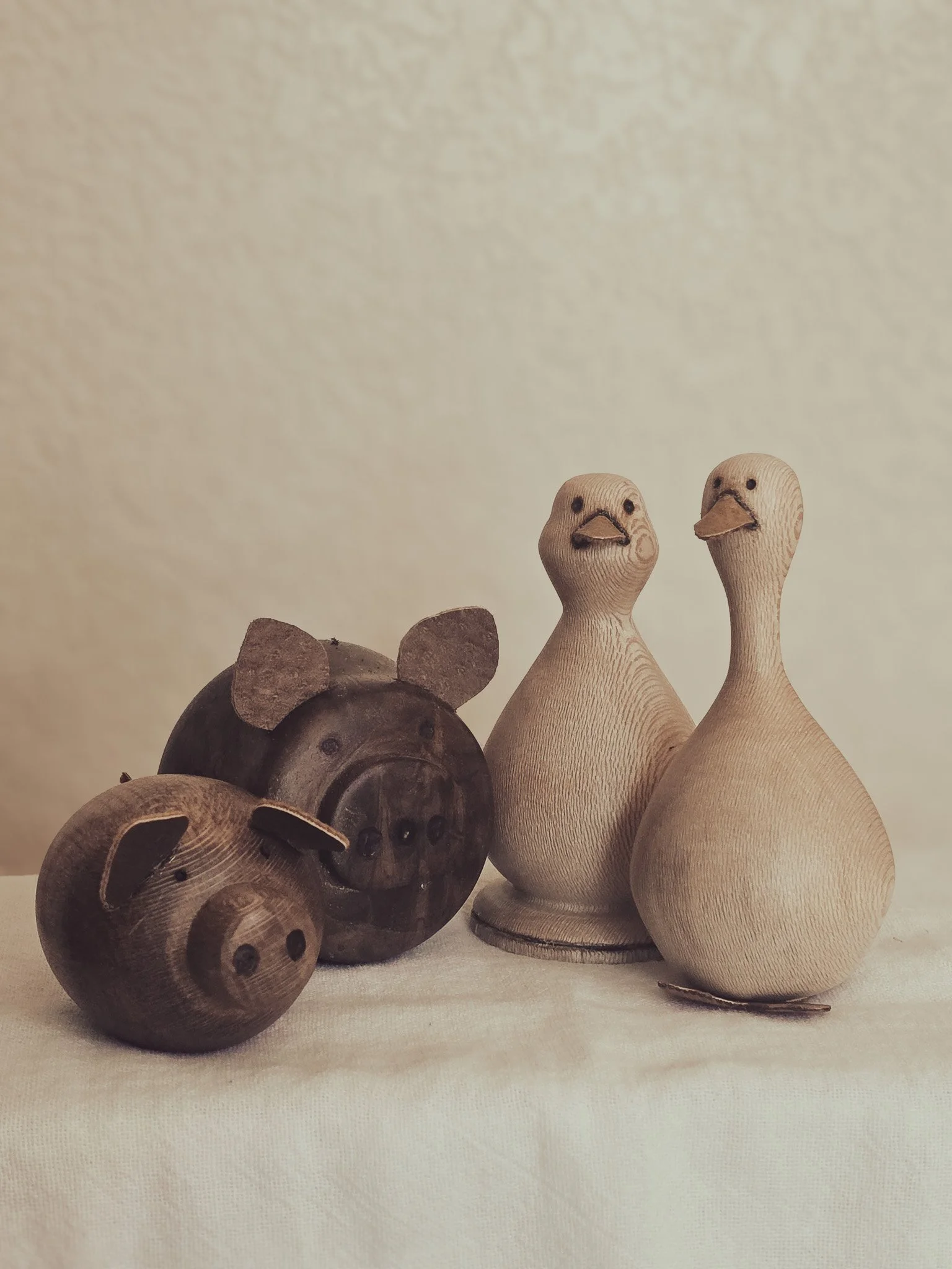 Wooden animal figurines resembling two pigs, a duck, and a goose are placed on a light-colored fabric surface.
