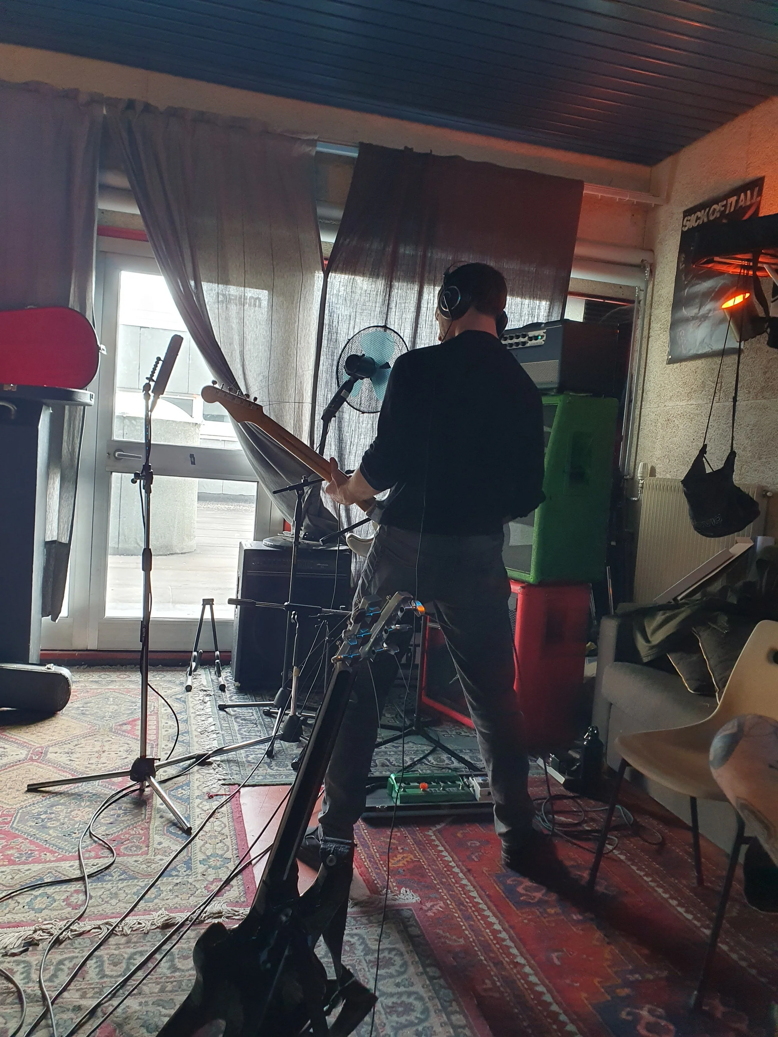 Una persona che suona la chitarra elettrica in un ambiente interno con strumenti musicali e attrezzature da registrazione.