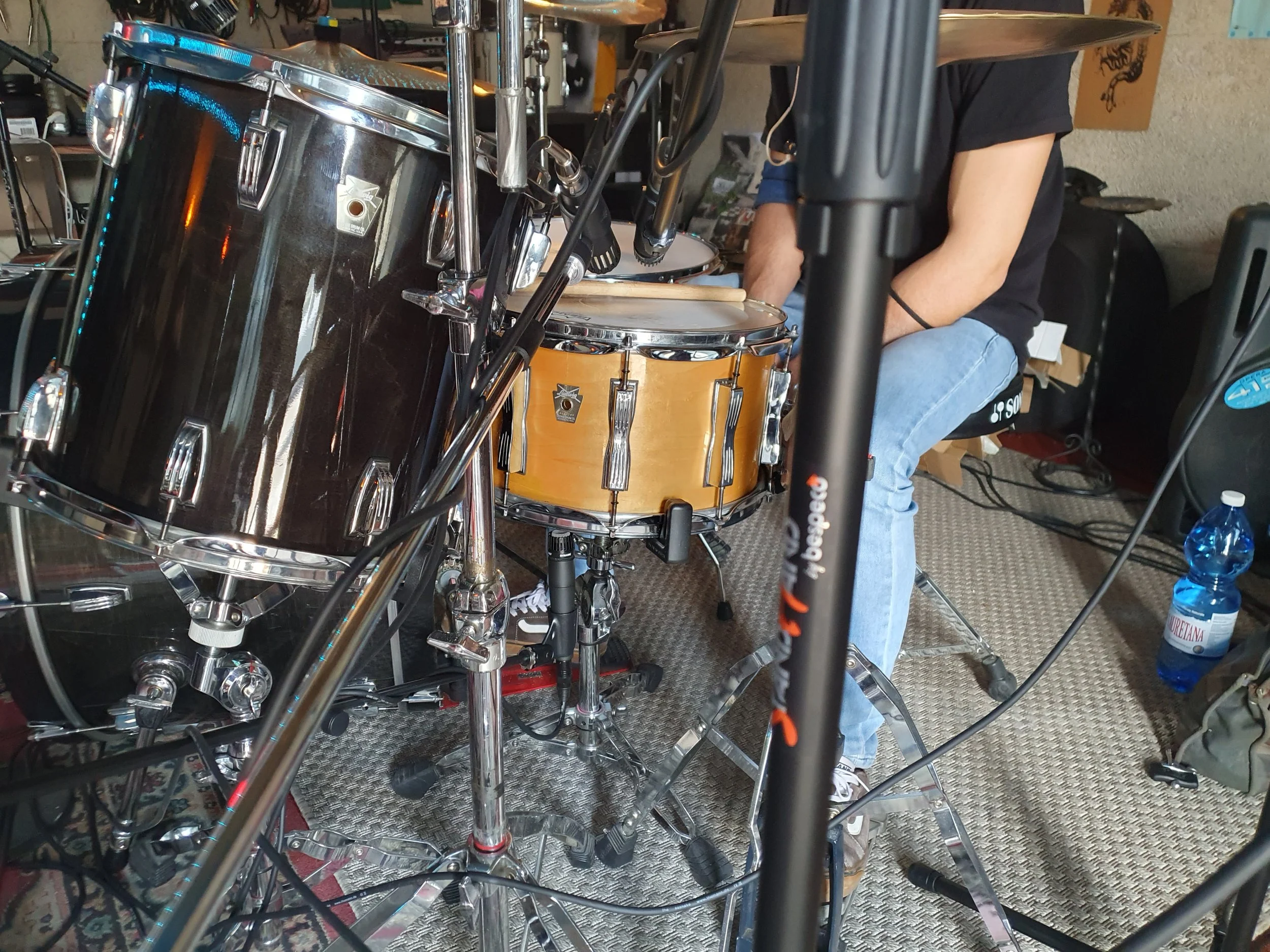 Batteria e timpani di una band musicale, con una persona seduta che si prepara a suonare, in un ambiente di studio o prova musicale