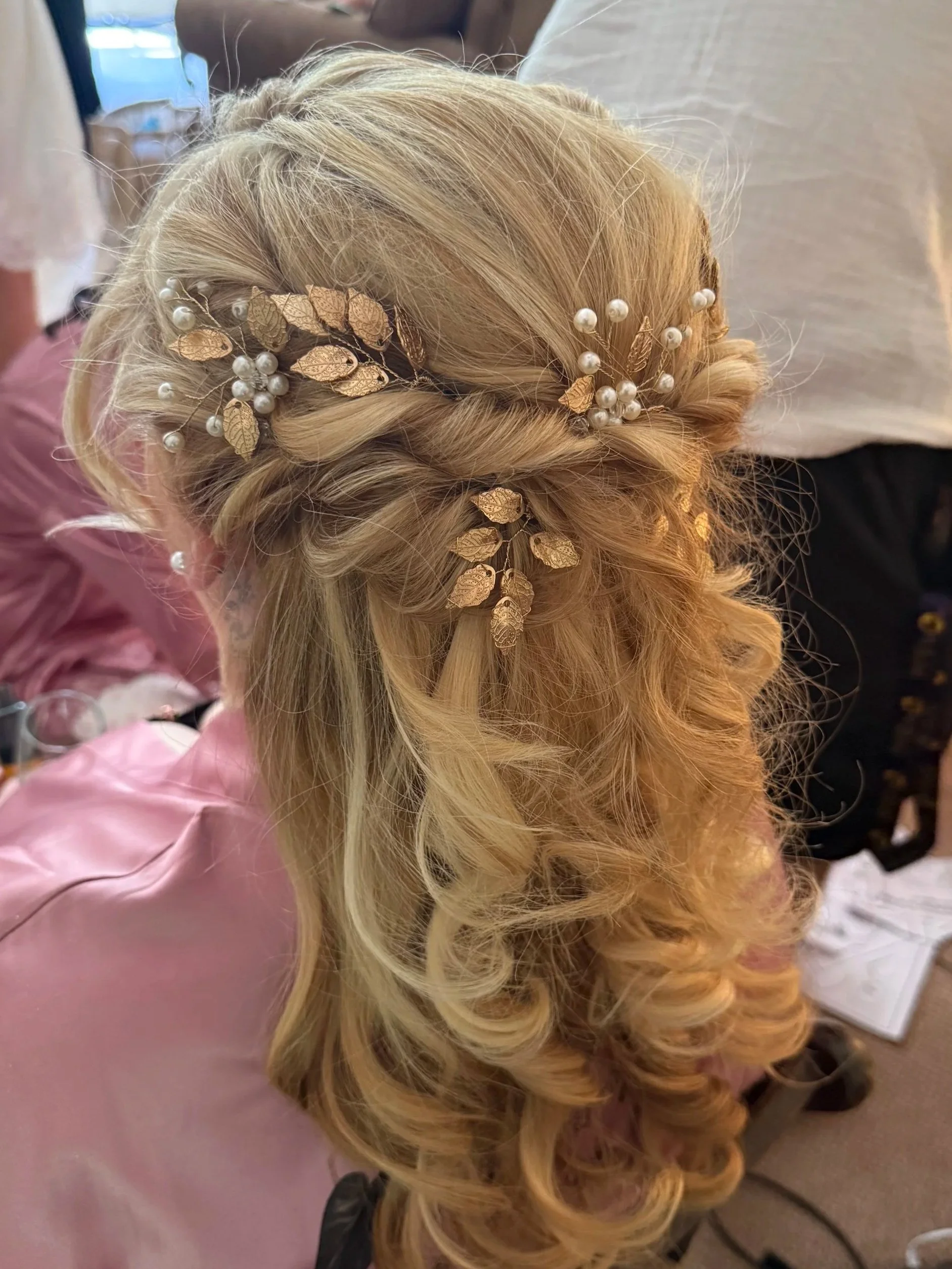 Blonde hair styled in loose curls with gold and pearl decorative hair accessories.