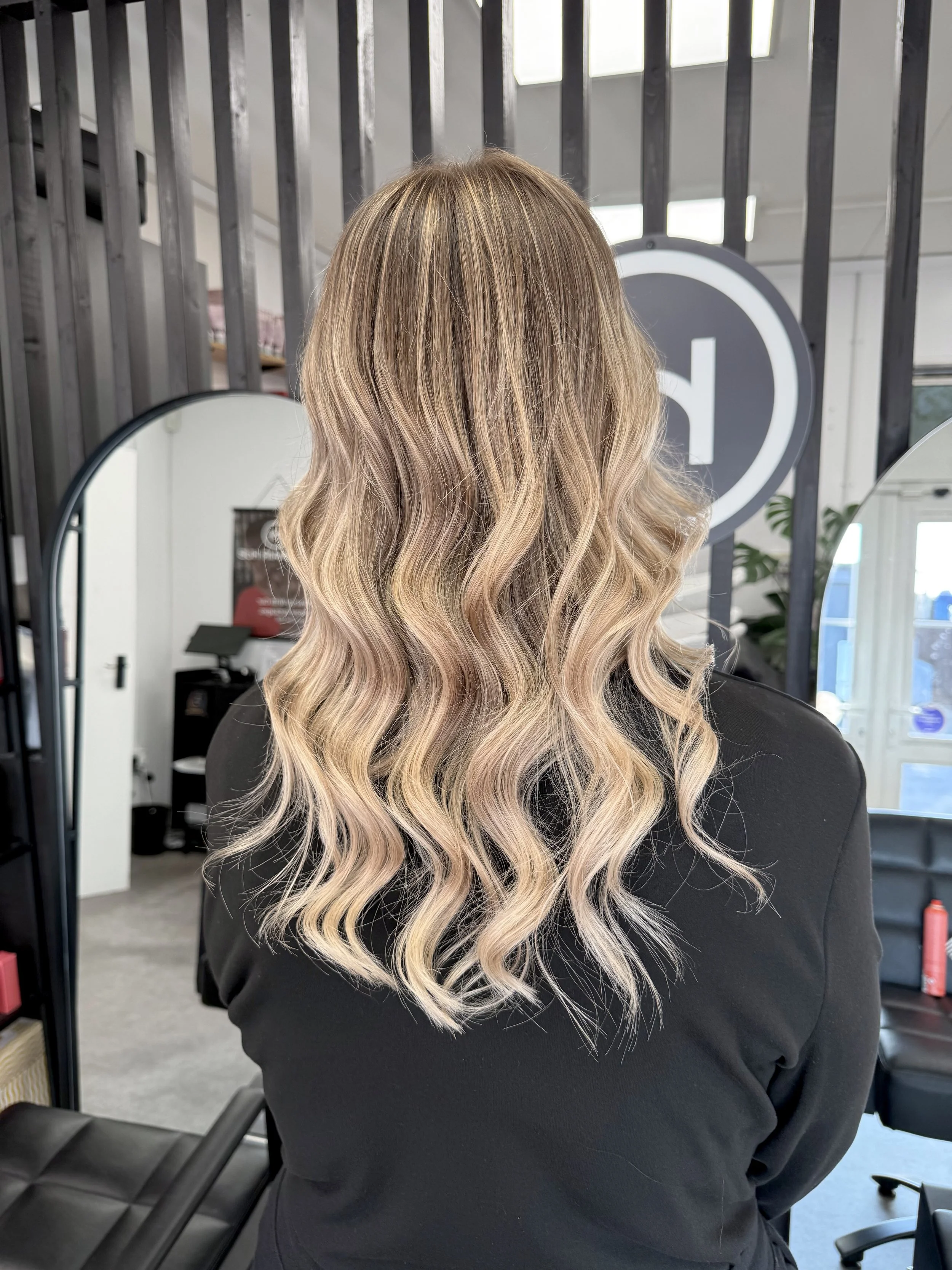 Back view of woman with long, wavy blonde hair in a salon.