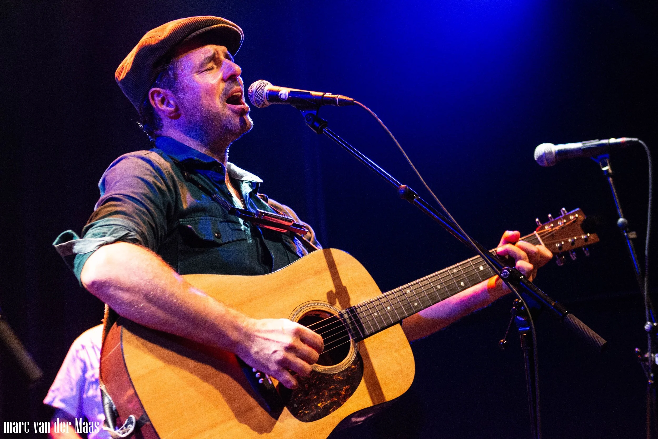 Dieter van der Westen playing an acoustic guitar on stage with purple and blue lighting.