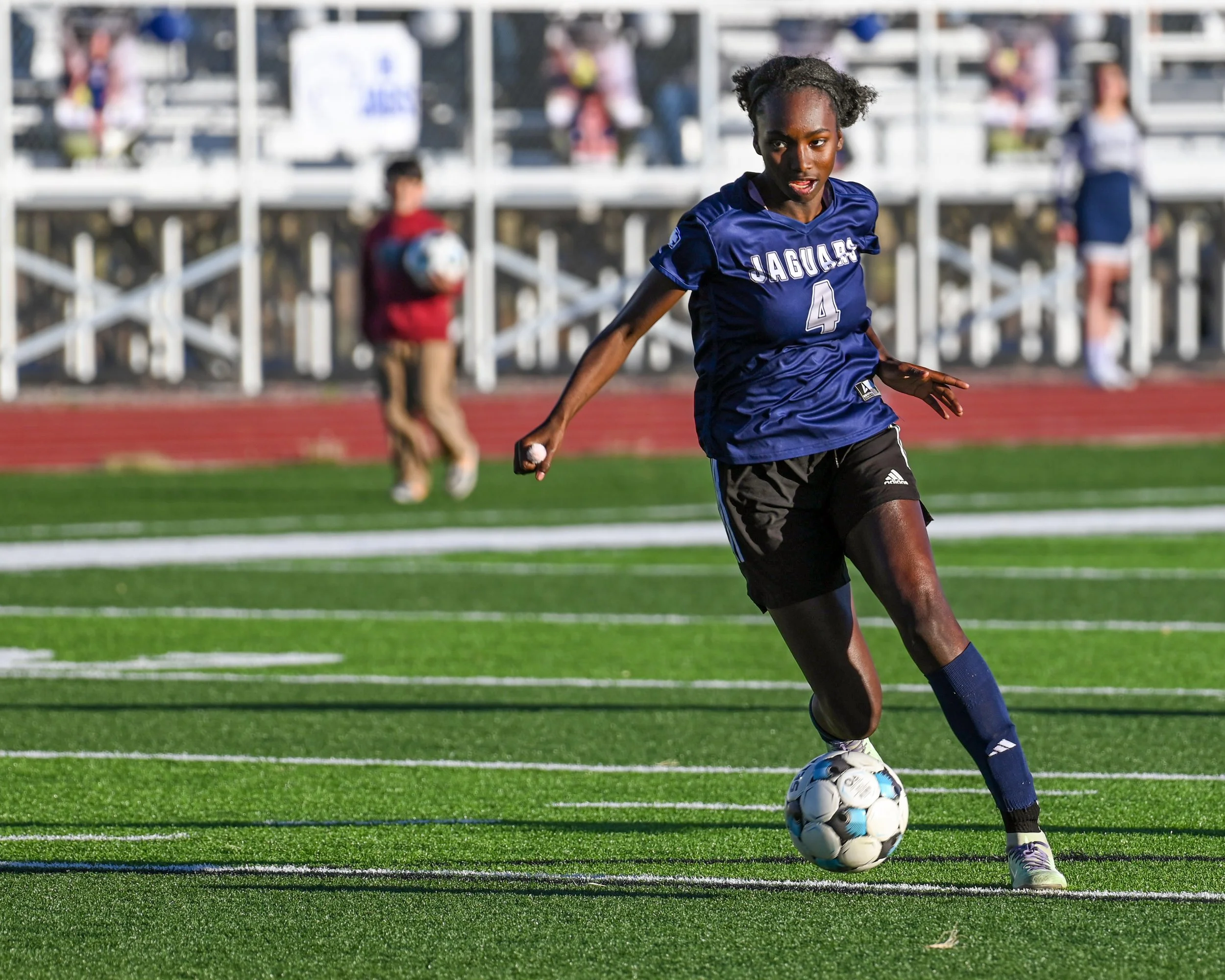 High school soccer forward dribbling the soccer ball across the green field, making a cut towards the goal, poised to take the decisive shot.