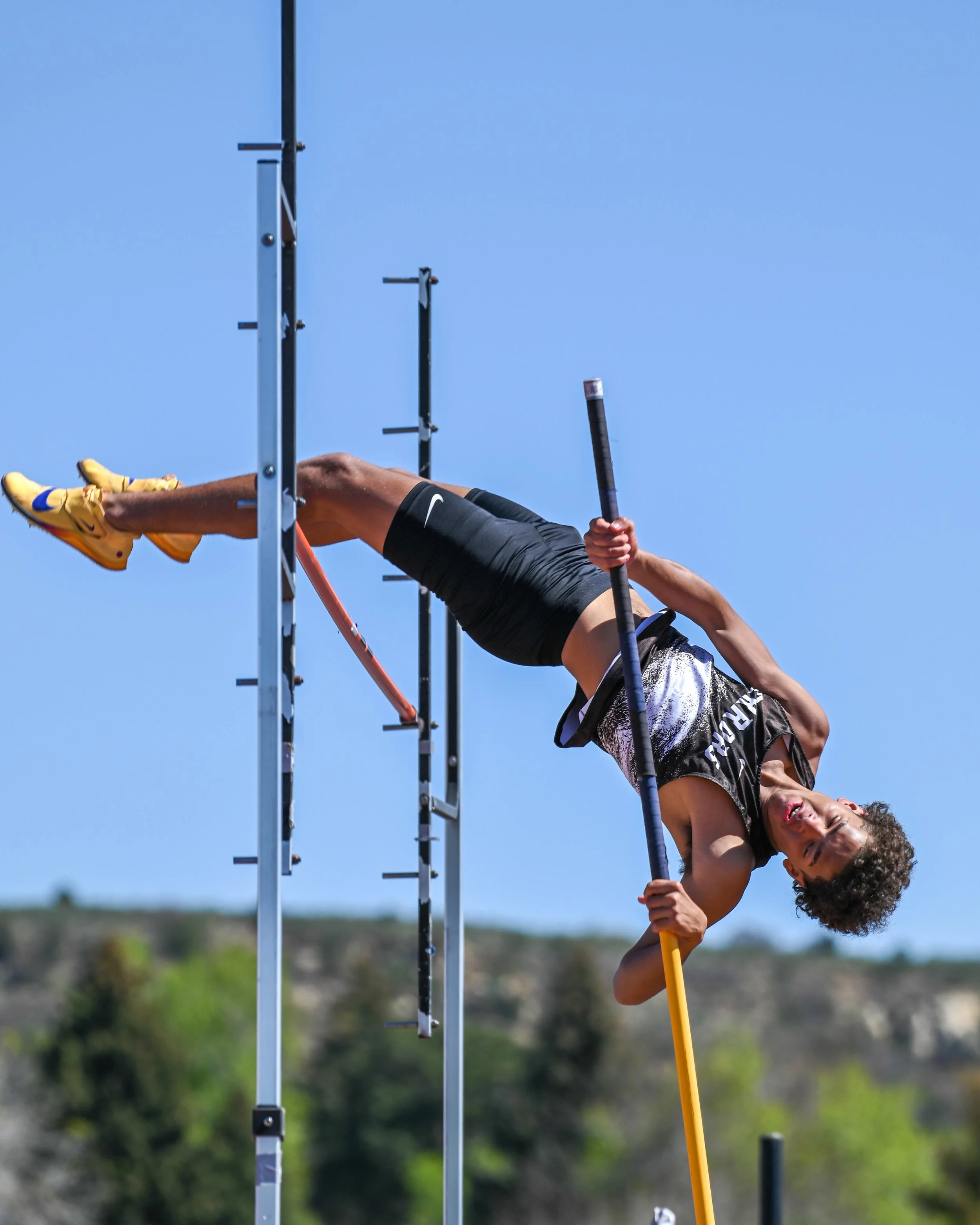 A male athlete competing in the pole vault outdoors against a clear blue sky in the background.