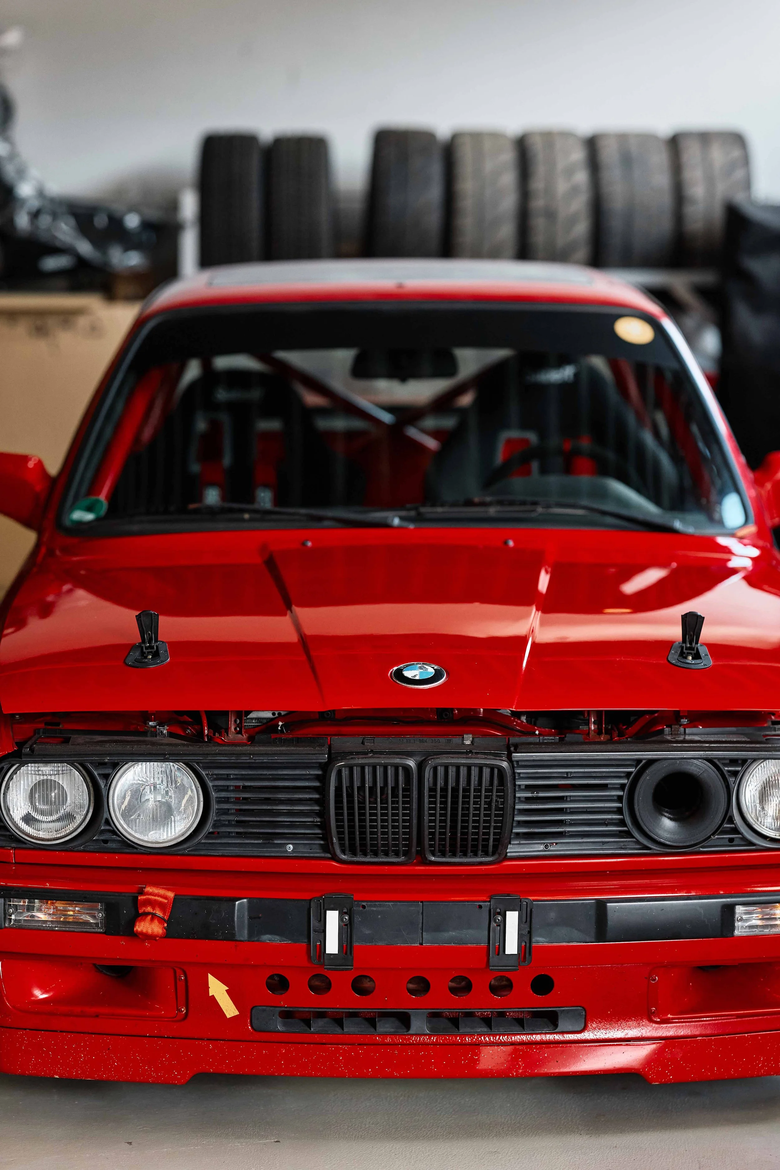Vorderansicht eines roten BMW Rennwagens, offen stehende Motorhaube, mit Reifenstapeln im Hintergrund.