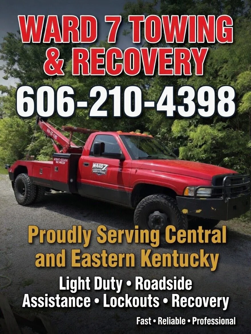 A red tow truck with black bumper parked on a road with green trees in the background, advertising Ward 7 Towing & Recovery service in Kentucky, providing roadside assistance, lockouts, recovery, and family-owned service with contact number 606-210-4398.