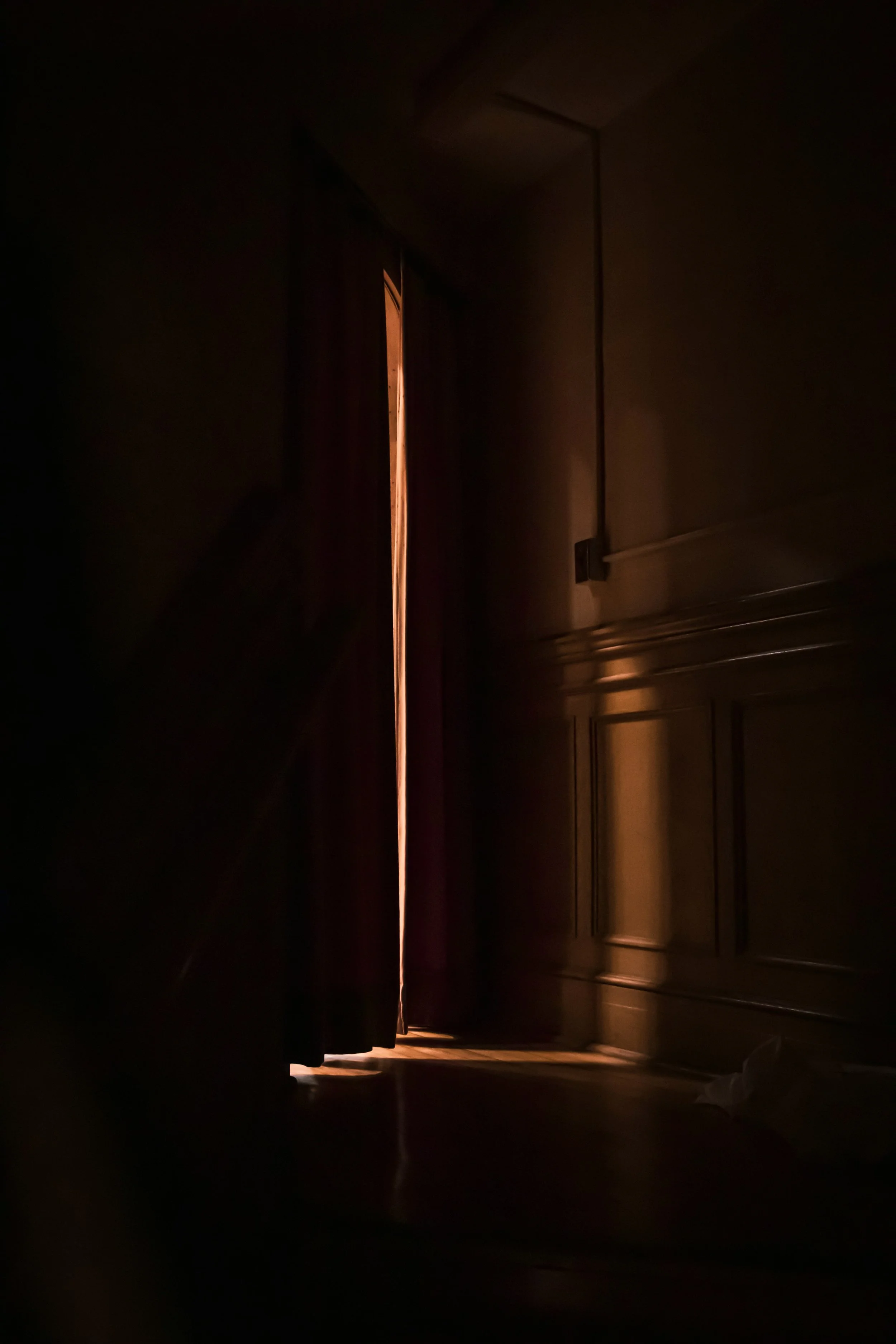 Dark theater with curtains slightly parted, revealing a small sliver of light coming from the stage.