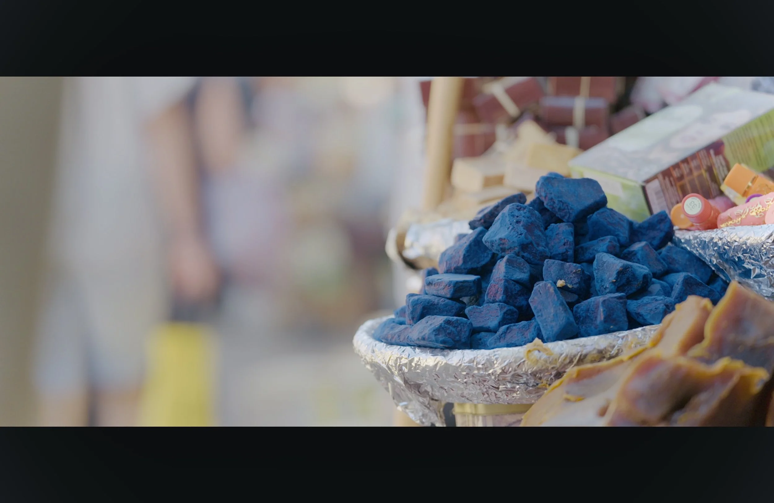 Colorful rocks, snacks, and packaged foods displayed on a table at an outdoor market or fair.