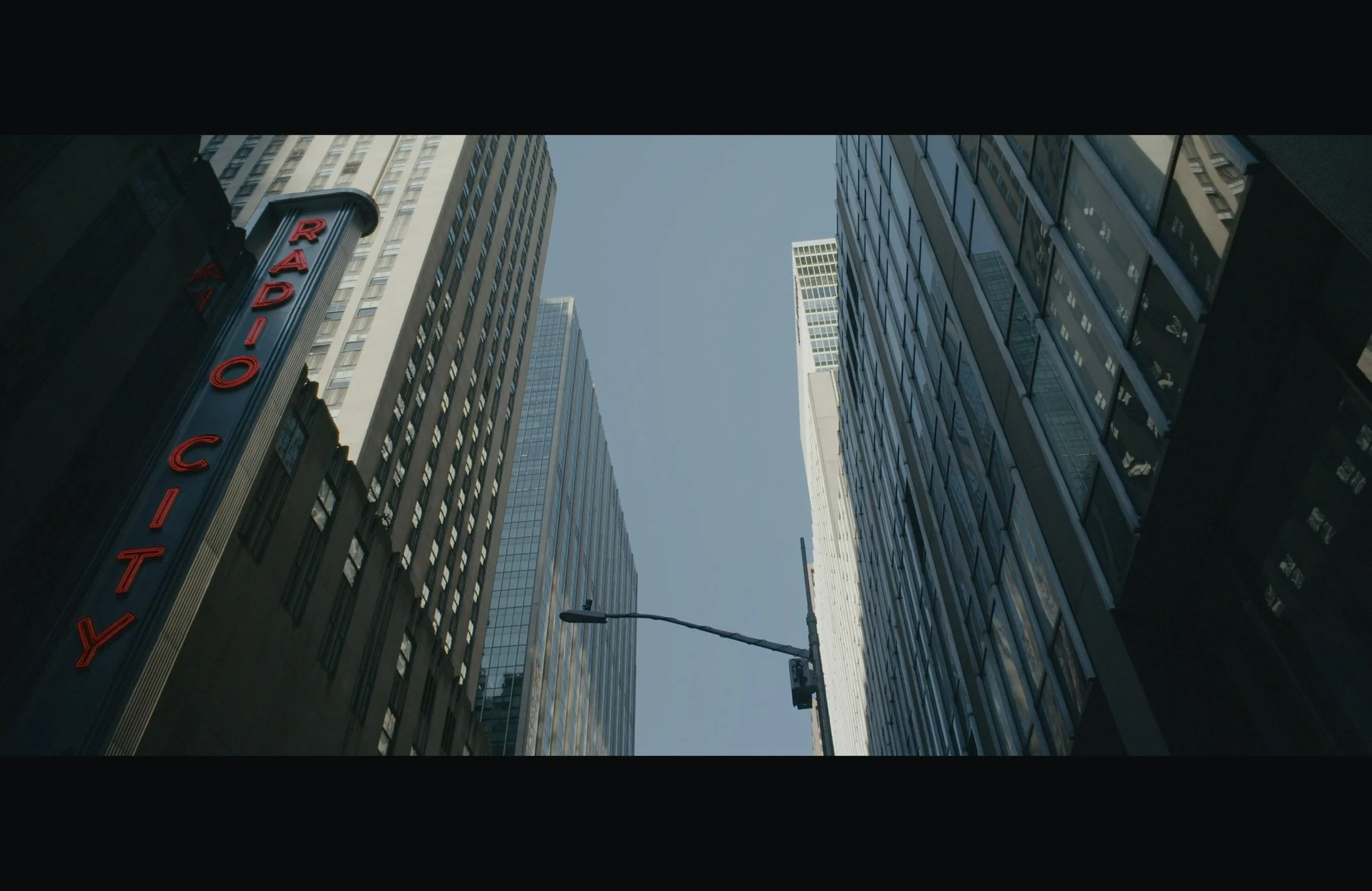 Tall skyscrapers with glass windows in a city, viewed from below, with a clear blue sky above, and a street with a lamppost in the foreground.