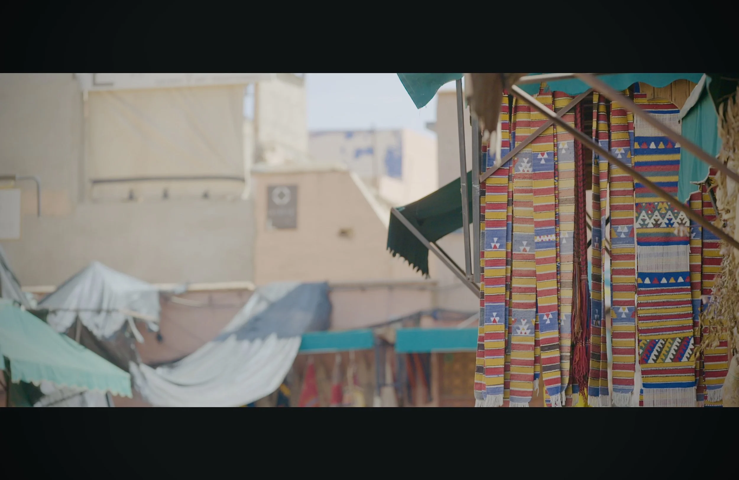 Colorful textiles hanging on a market stall, with a beige building in the background.