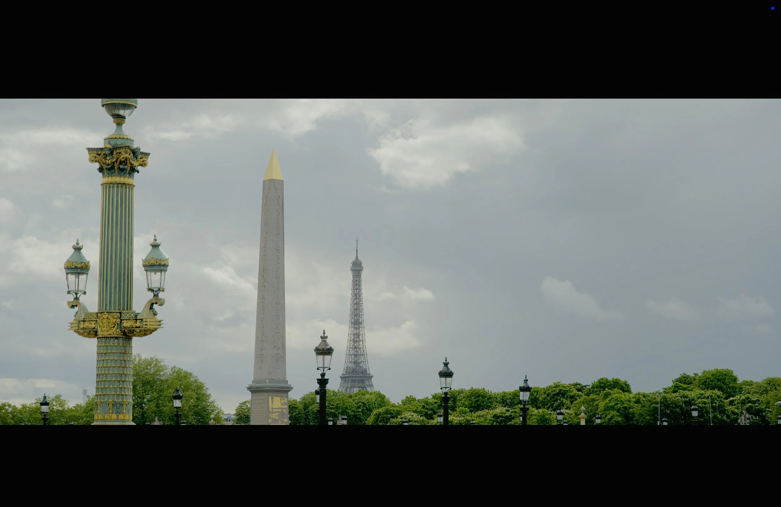 Paris skyline with the Eiffel Tower, an Egyptian obelisk, ornate street lamps, and a cloudy sky.