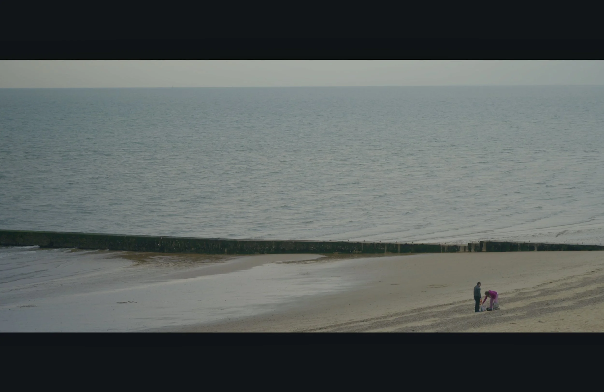 People on a beach near the water, with two children and an adult, possibly a parent, engaging in an activity near the shoreline.
