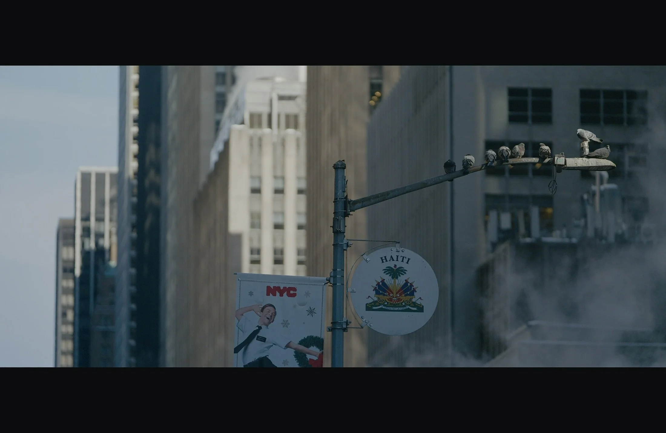Urban street scene with pigeon perched on a traffic light pole, billboard advertising NYC, and a building in the background.