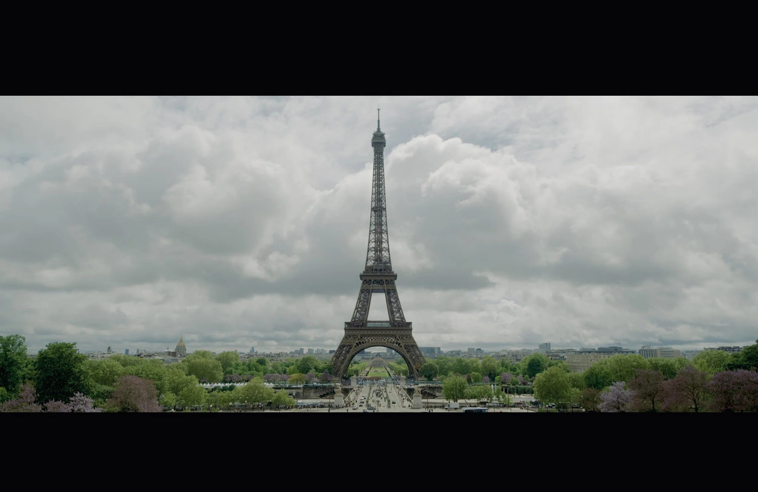 Eiffel Tower in Paris, France, with cloudy sky and green trees in foreground.