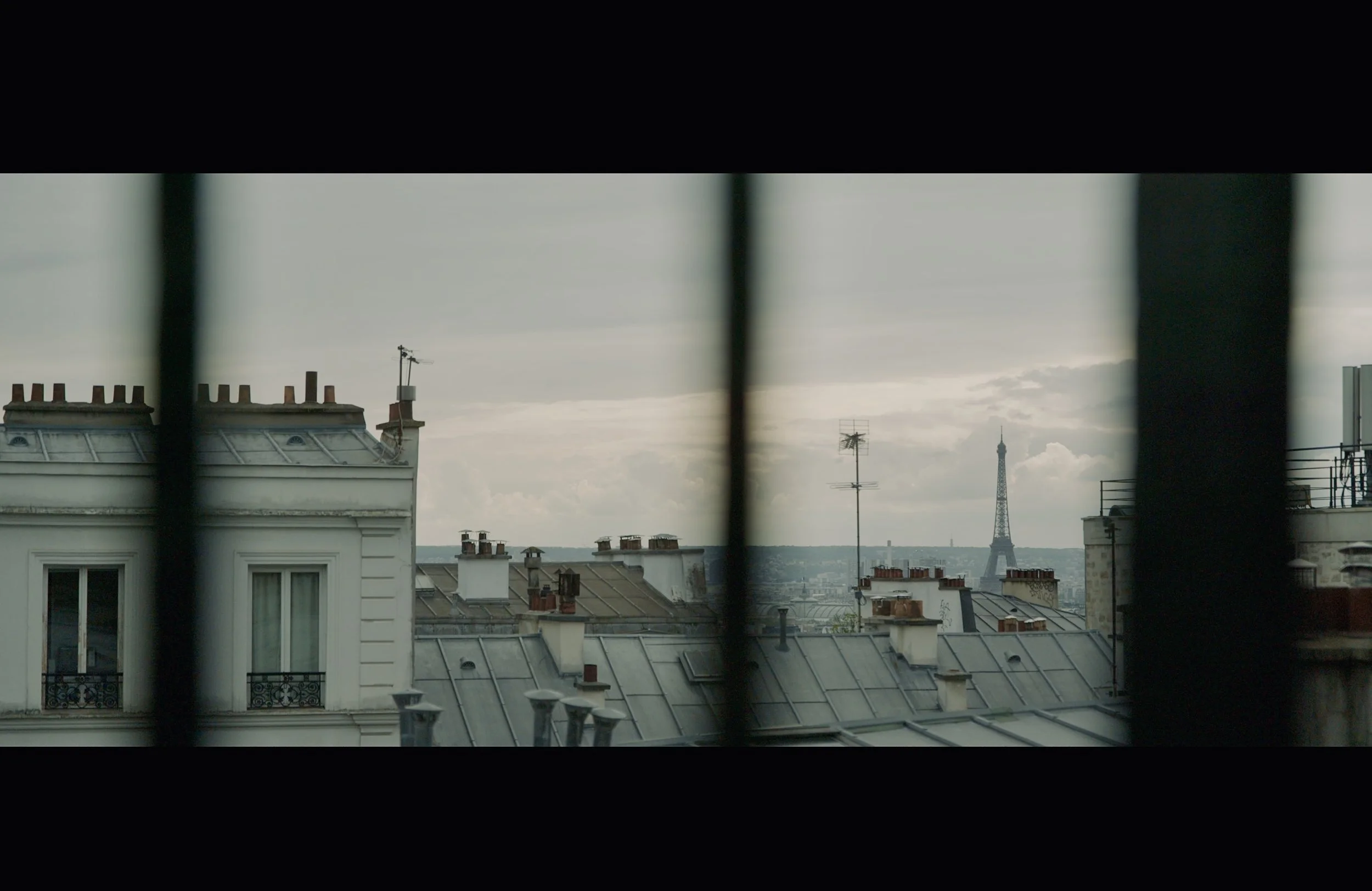 View of Paris rooftops with chimneys, antennas, and the Eiffel Tower in the background.