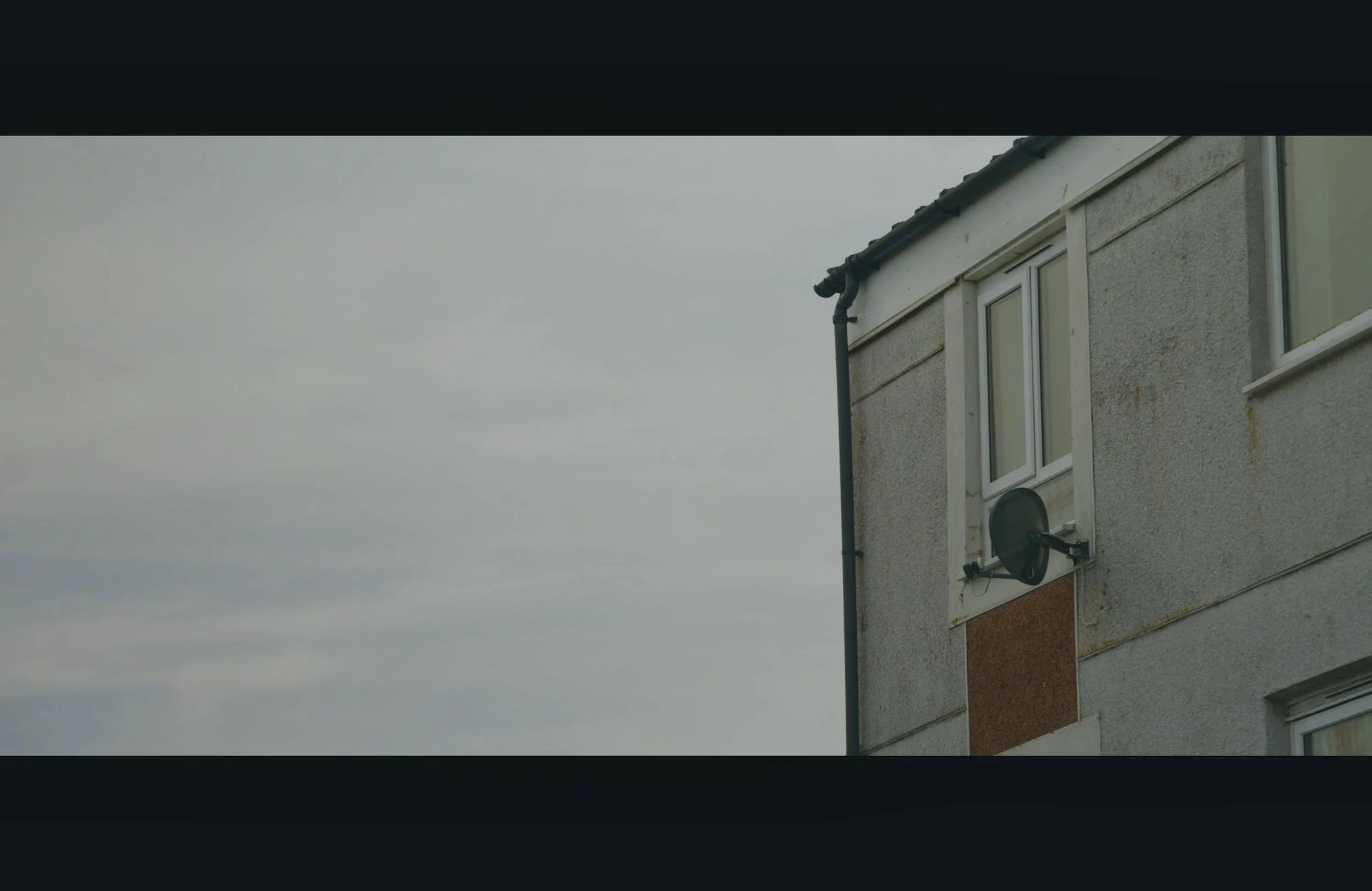Close-up of a residential building with windows and a satellite dish, under an overcast sky.