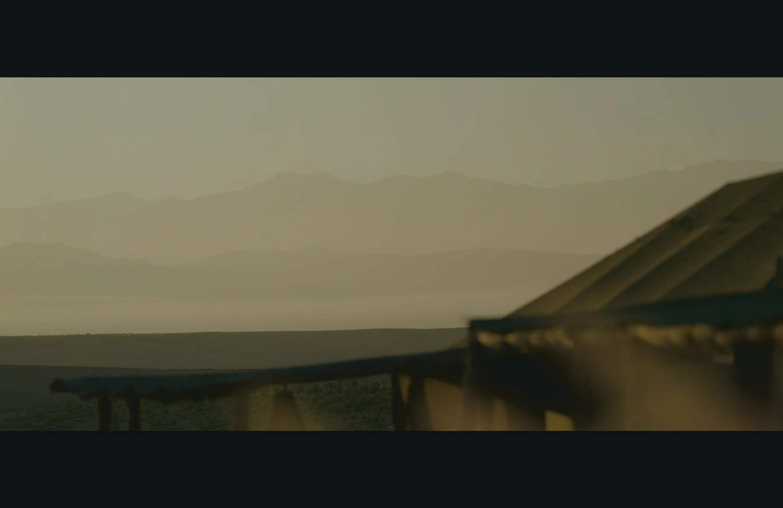 A blurred landscape with mountains in the distance and a structure with a roof in the foreground.