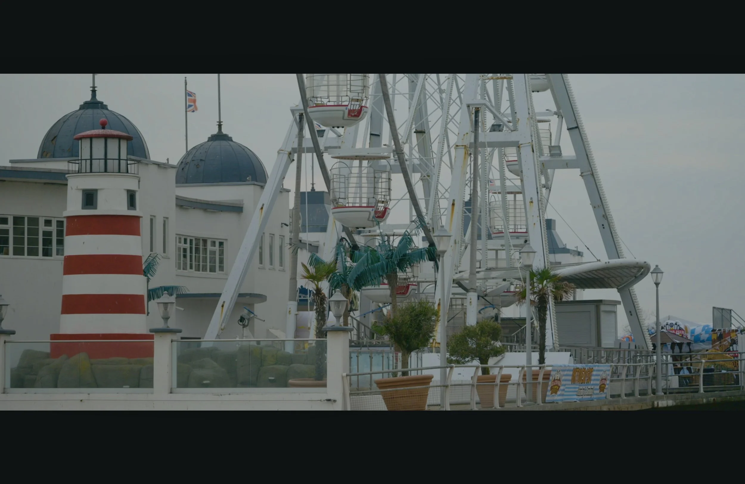 A Ferris wheel at an amusement park with a building featuring domed roofs and a lighthouse with red and white stripes in the foreground.
