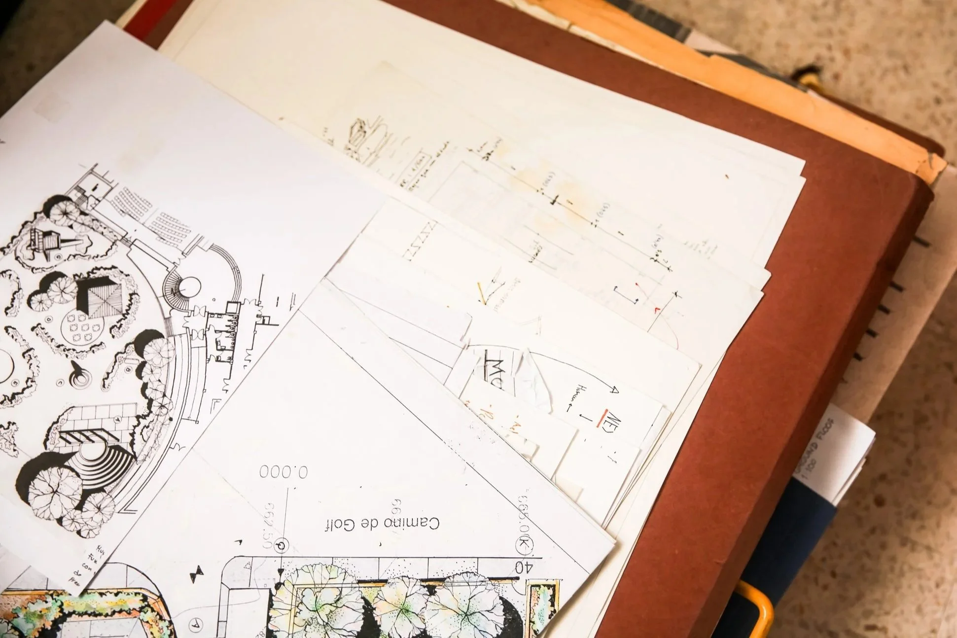 Architectural plans and drawings spread out on a wooden table, partially overlapping each other.
