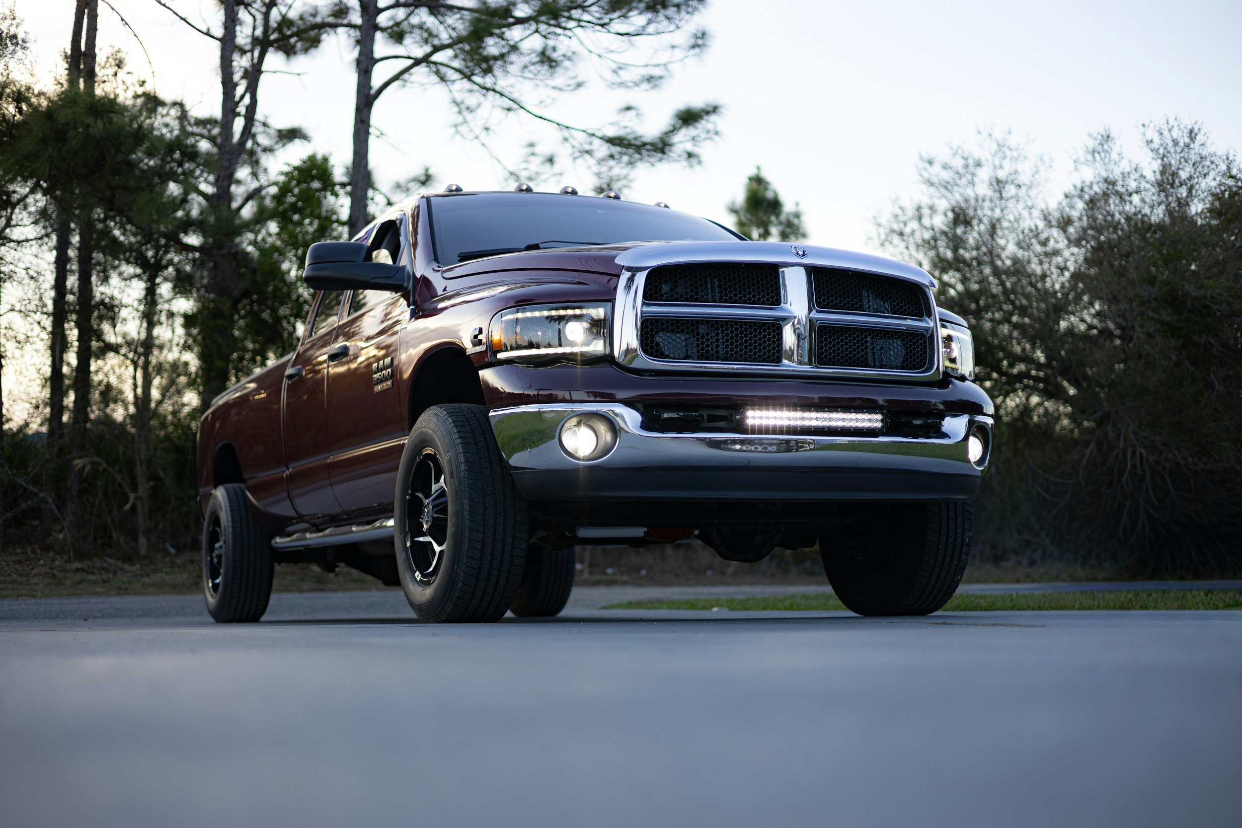 A dark red Dodge Ram 2500 truck with chrome accents parked outdoors during daylight, with trees and partly cloudy skies in the background.