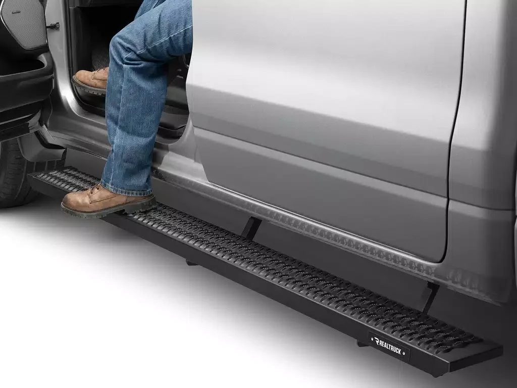 Person wearing jeans and brown shoes stepping into a silver pickup truck with a black running board.