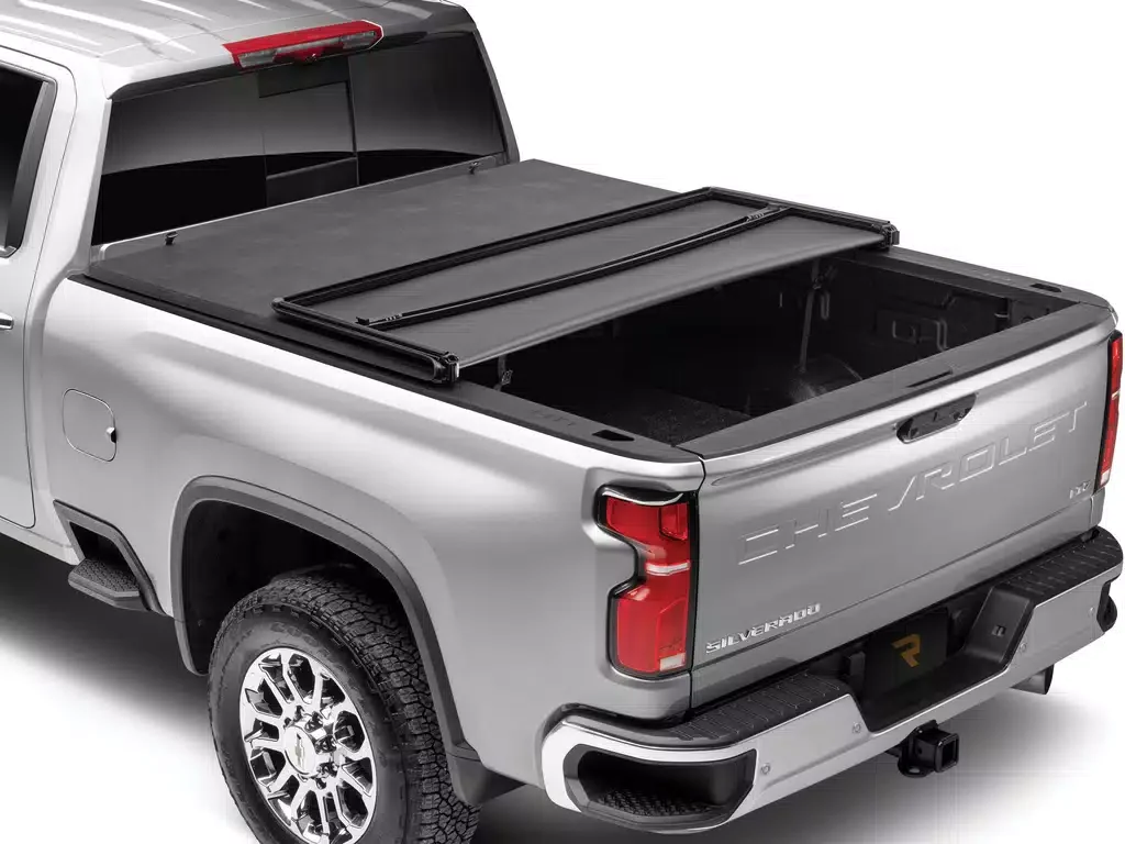 Rear view of a silver Chevrolet Silverado pickup truck with the tailgate down, showing an empty truck bed and a retractable tonneau cover partially opened.