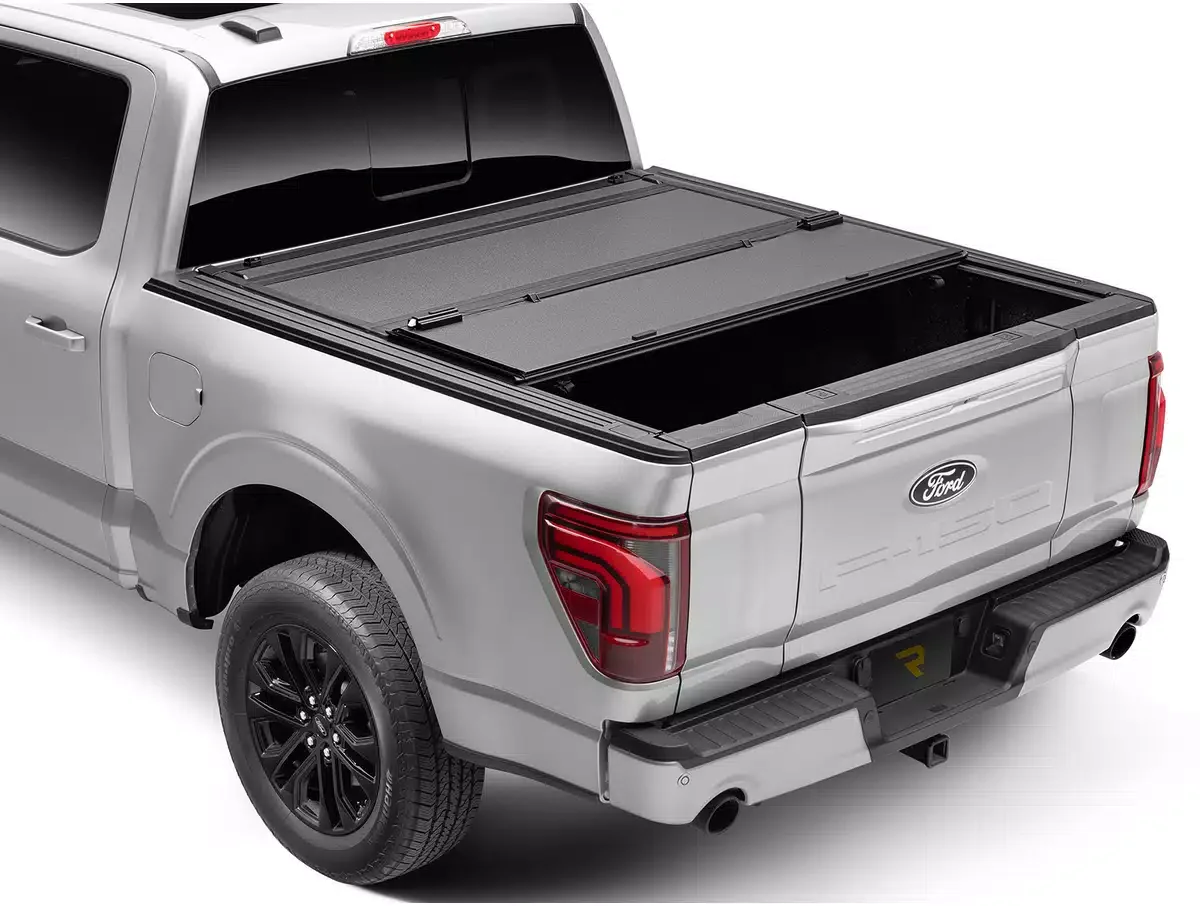Silver Ford pickup truck with an open bed, showing a tonneau cover partially retracted over the bed, and black wheels.
