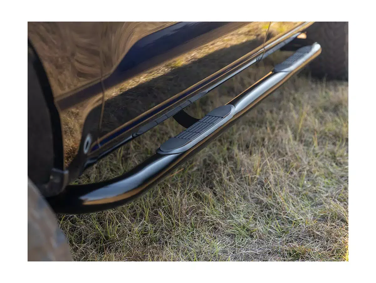 Close-up of a vehicle's side step with a textured grip, mounted under the vehicle's door, on grassy ground.