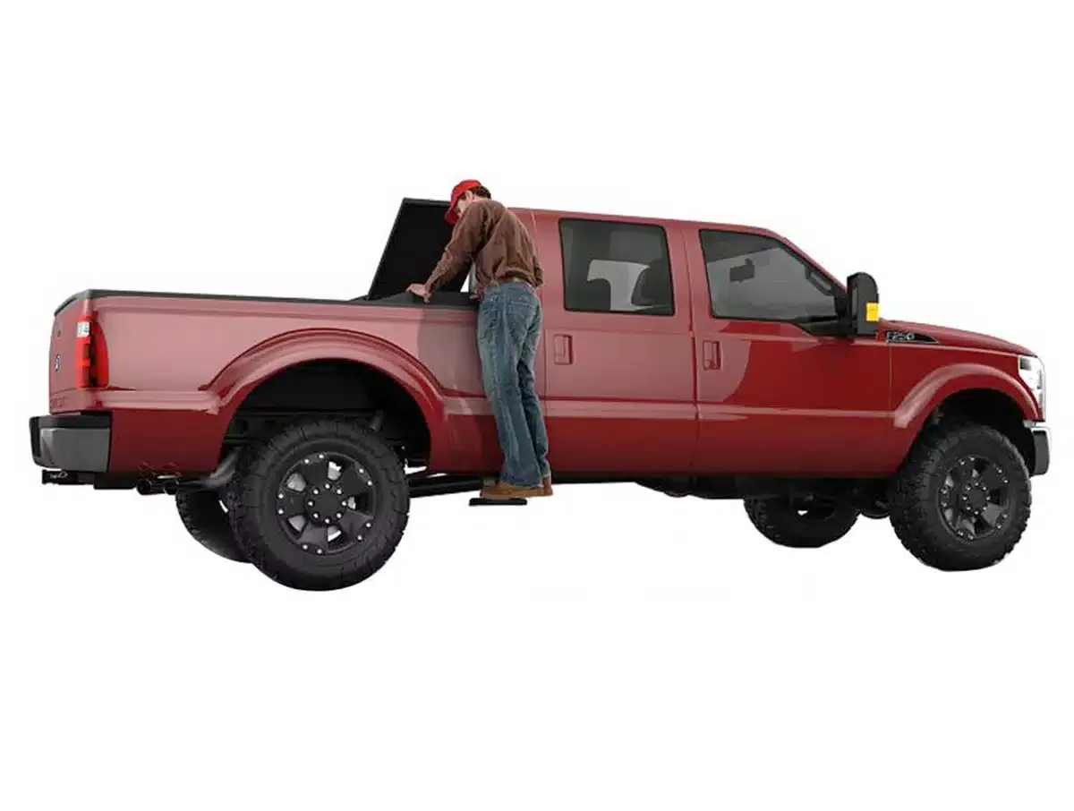 A person standing on a step stool, leaning into the open hood of a red pickup truck.