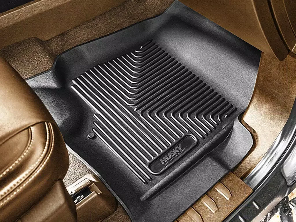 Black rubber Husky floor liner on tan carpet in a vehicle interior.