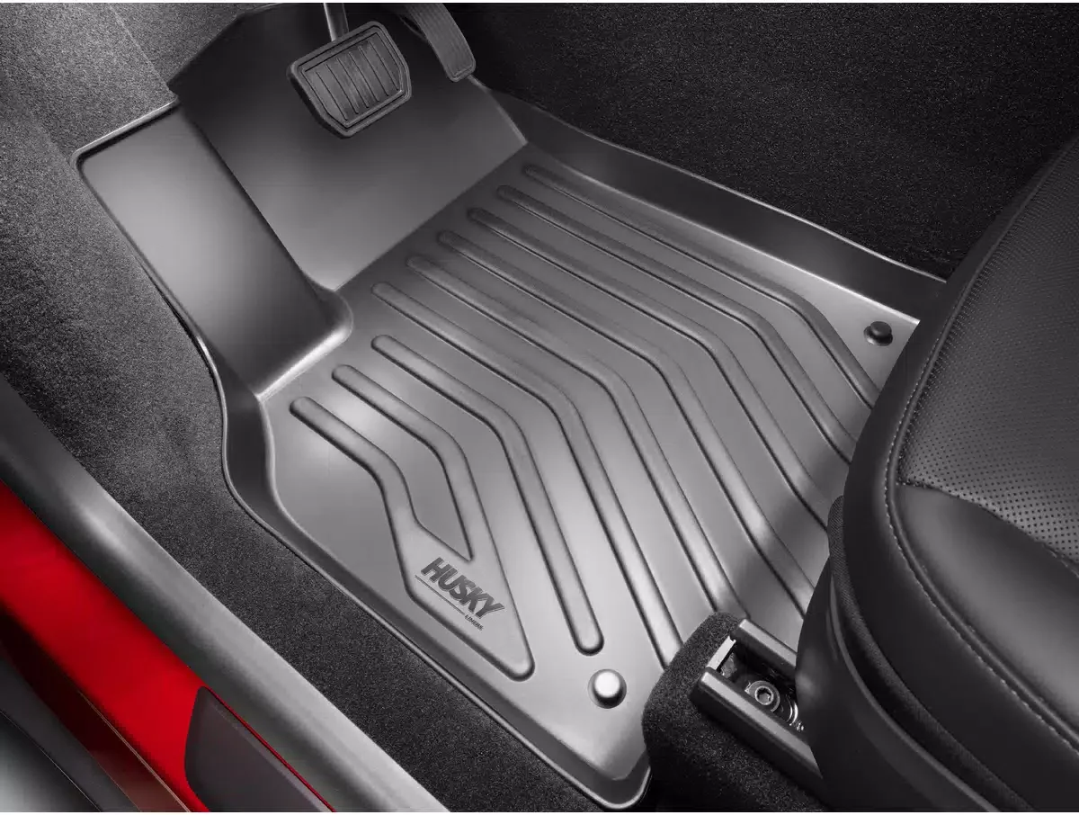 Car floor mat with the brand name 'HUSKY' placed in the driver's side footwell, near the accelerator pedal and seat.