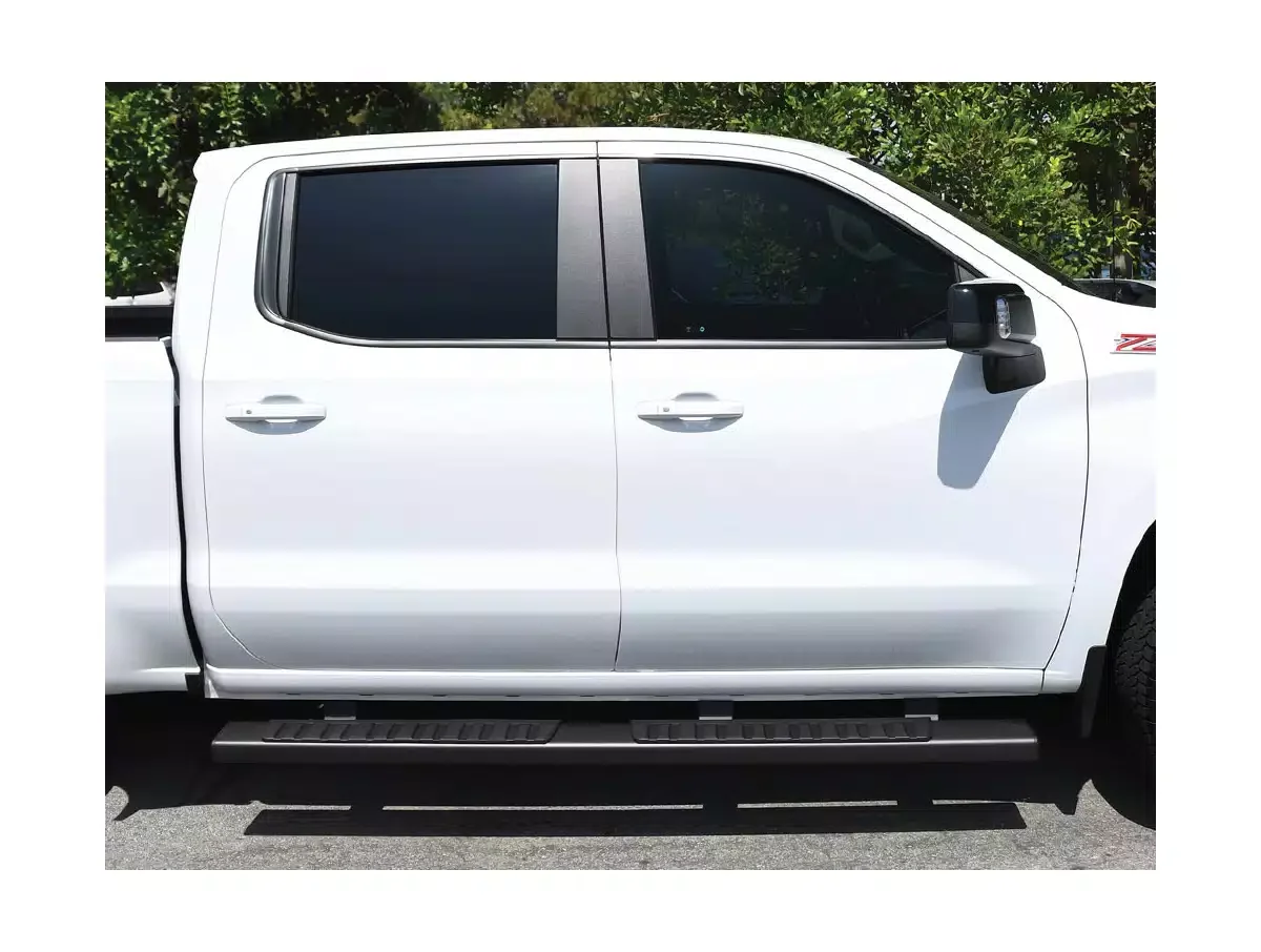 Side view of a white pickup truck with tinted windows and black side steps, parked outdoors with green trees in the background.