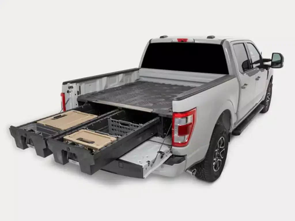 A silver pickup truck with the tailgate and side panels open, revealing a hidden compartment inside the bed that has storage boxes and electronic components.