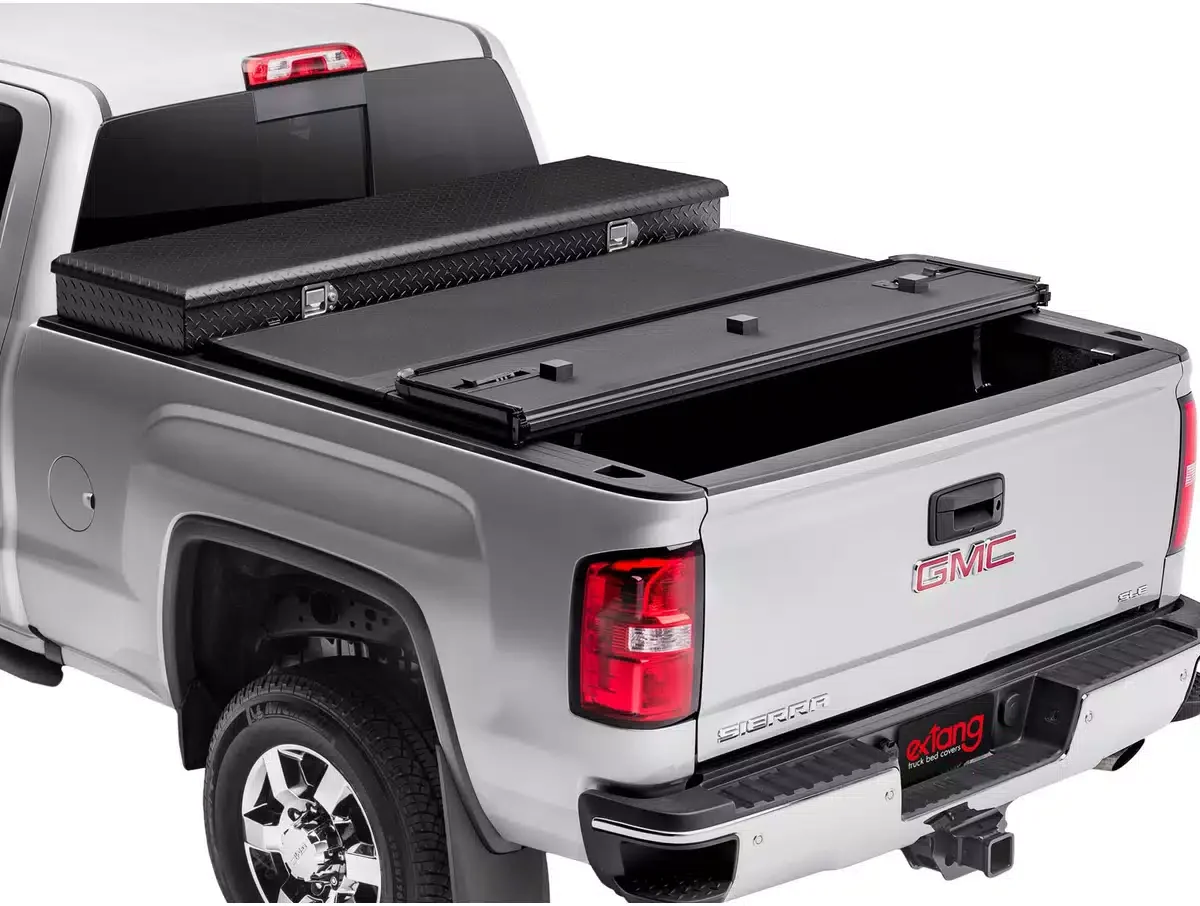 Silver GMC Sierra pickup truck with a black truck bed cover and storage box, and a spare tire mounted on the tailgate.
