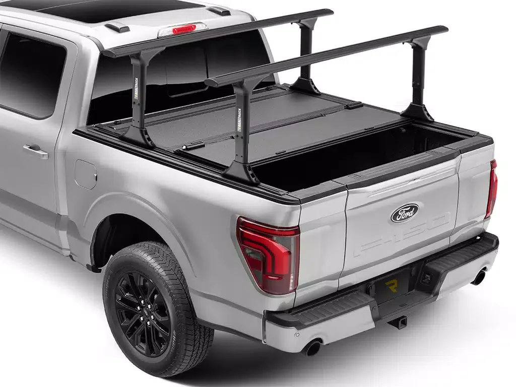 A silver Ford pickup truck with a black roof and black rims, featuring an additional custom roof rack over the bed for carrying long items.