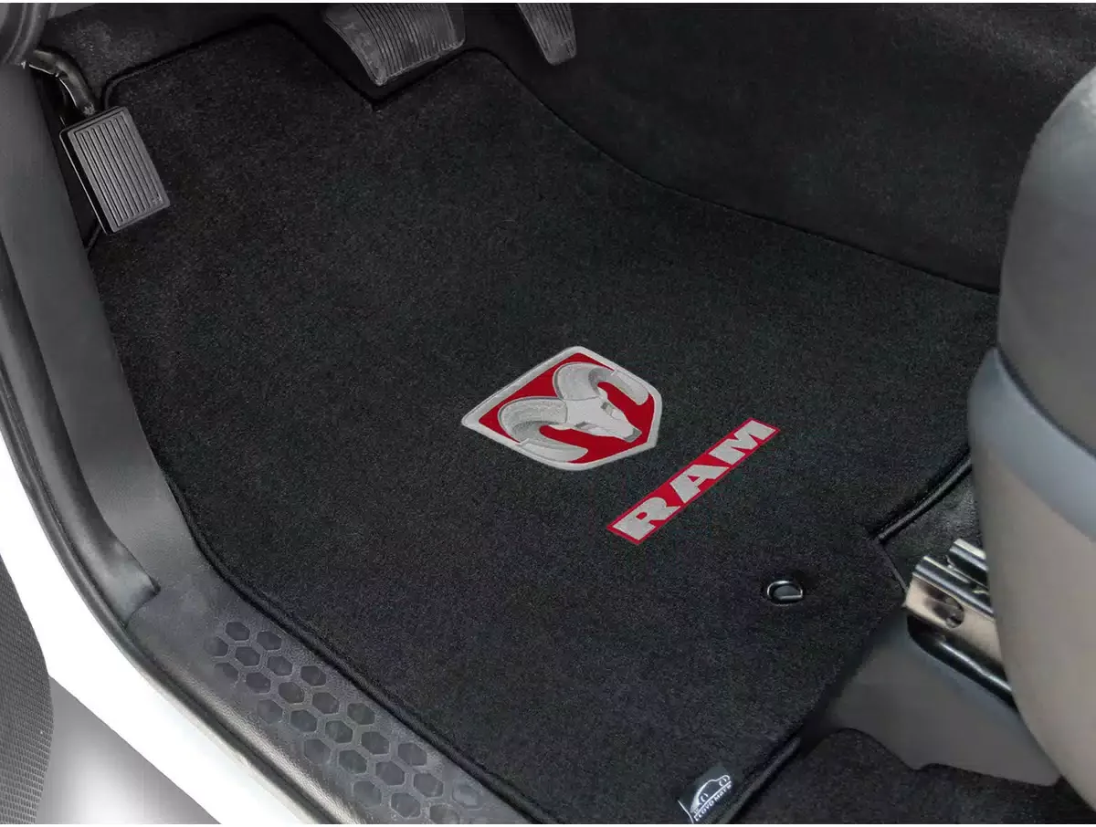 Black car floor mat with RAM logo and a silver ram head emblem, located on the driver side of the vehicle.