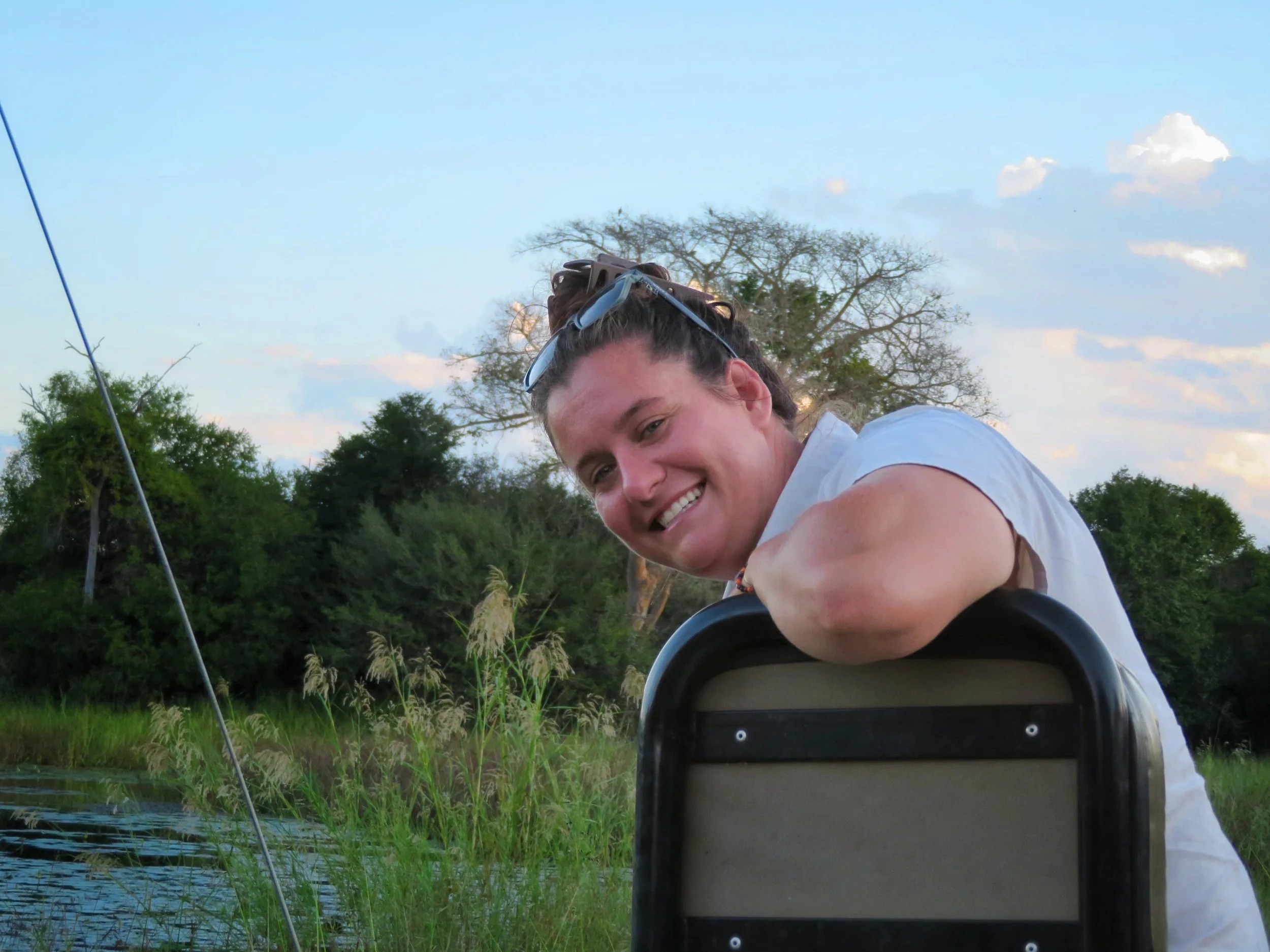 A smiling woman with sunglasses on her head is sitting on a tracker seat in houther africa