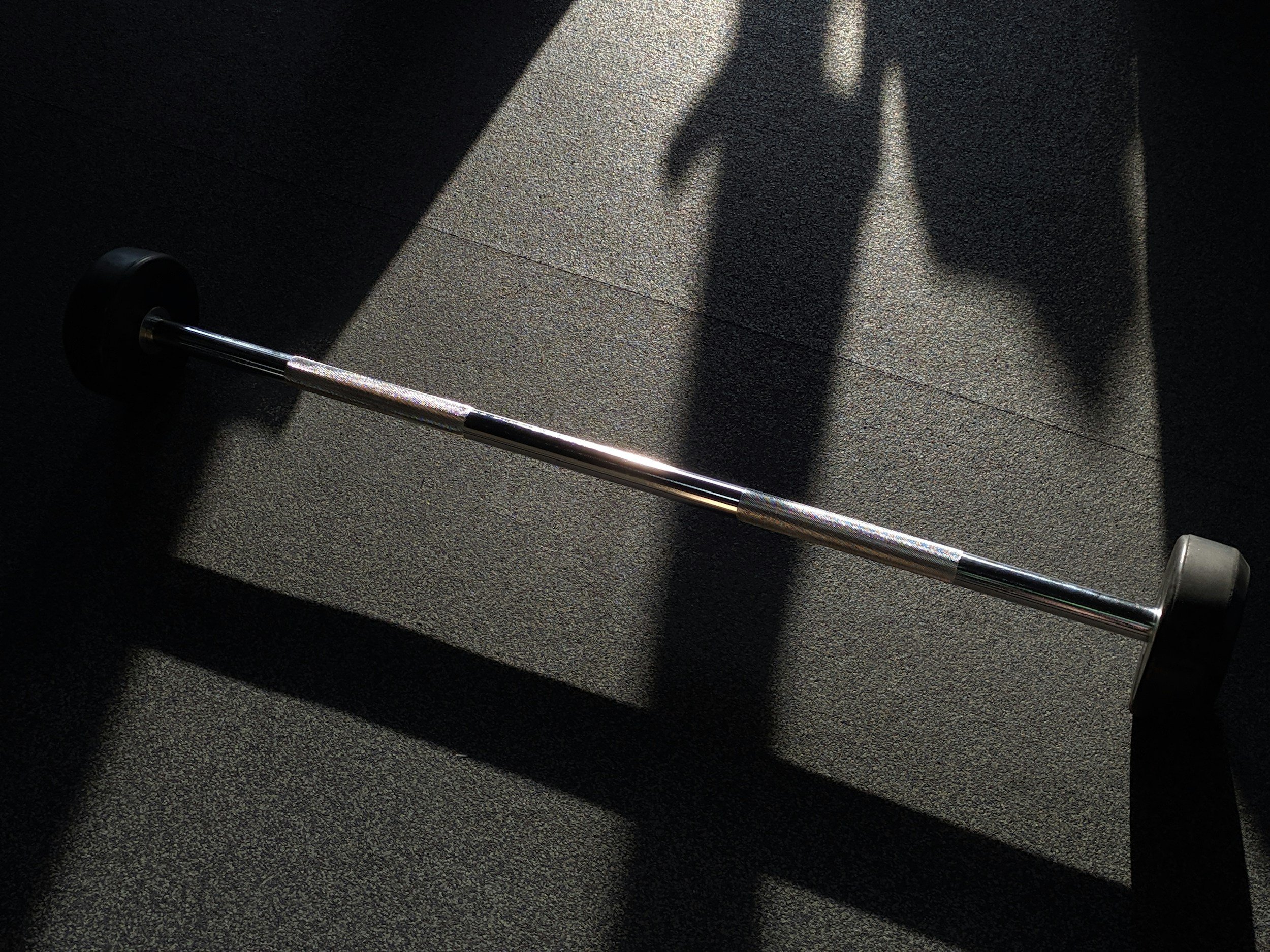 Shadow of a person standing on a textured floor next to a barbell.