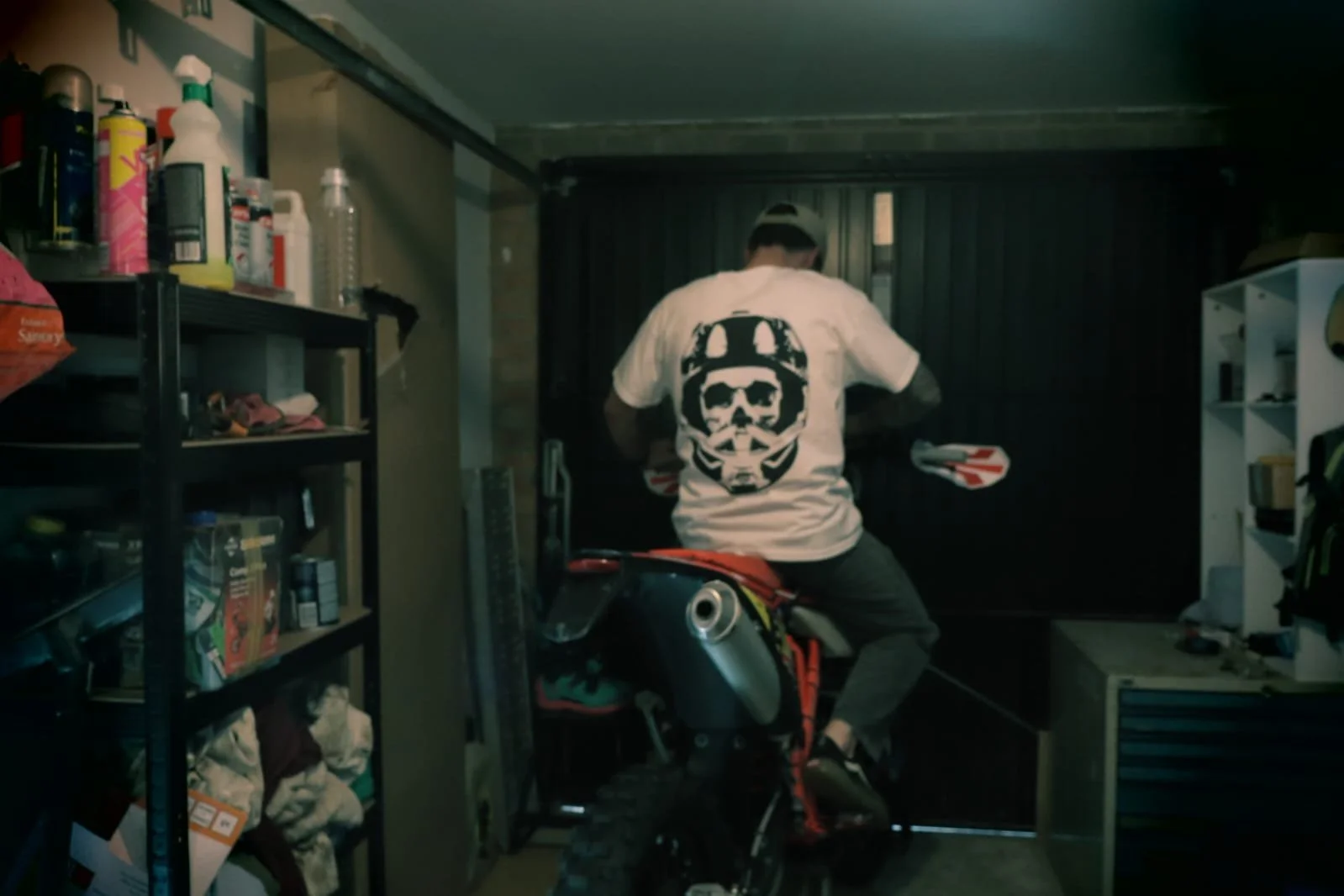 Man sitting on motocross enduro bike in garage wearing white moto skull t shirt