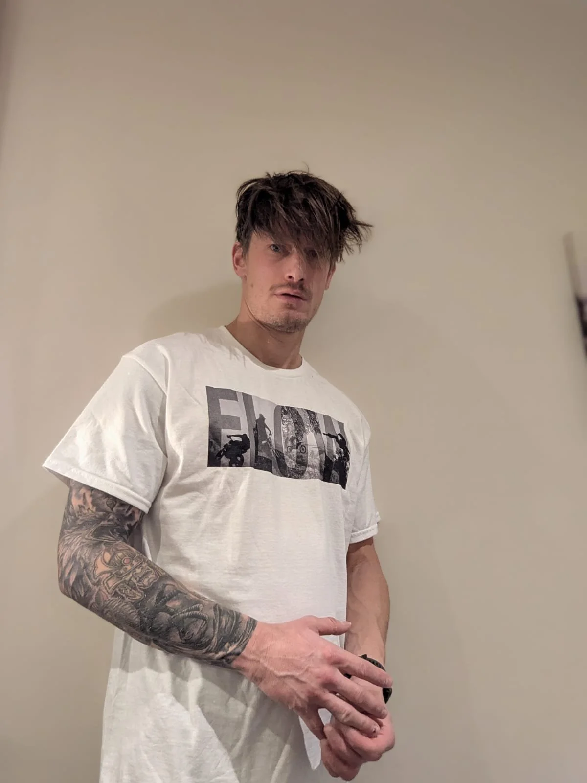 Man wearing white moto inspired t shirt with word 'flow' in the foreground and black and white imagery of dirt bikes in the background