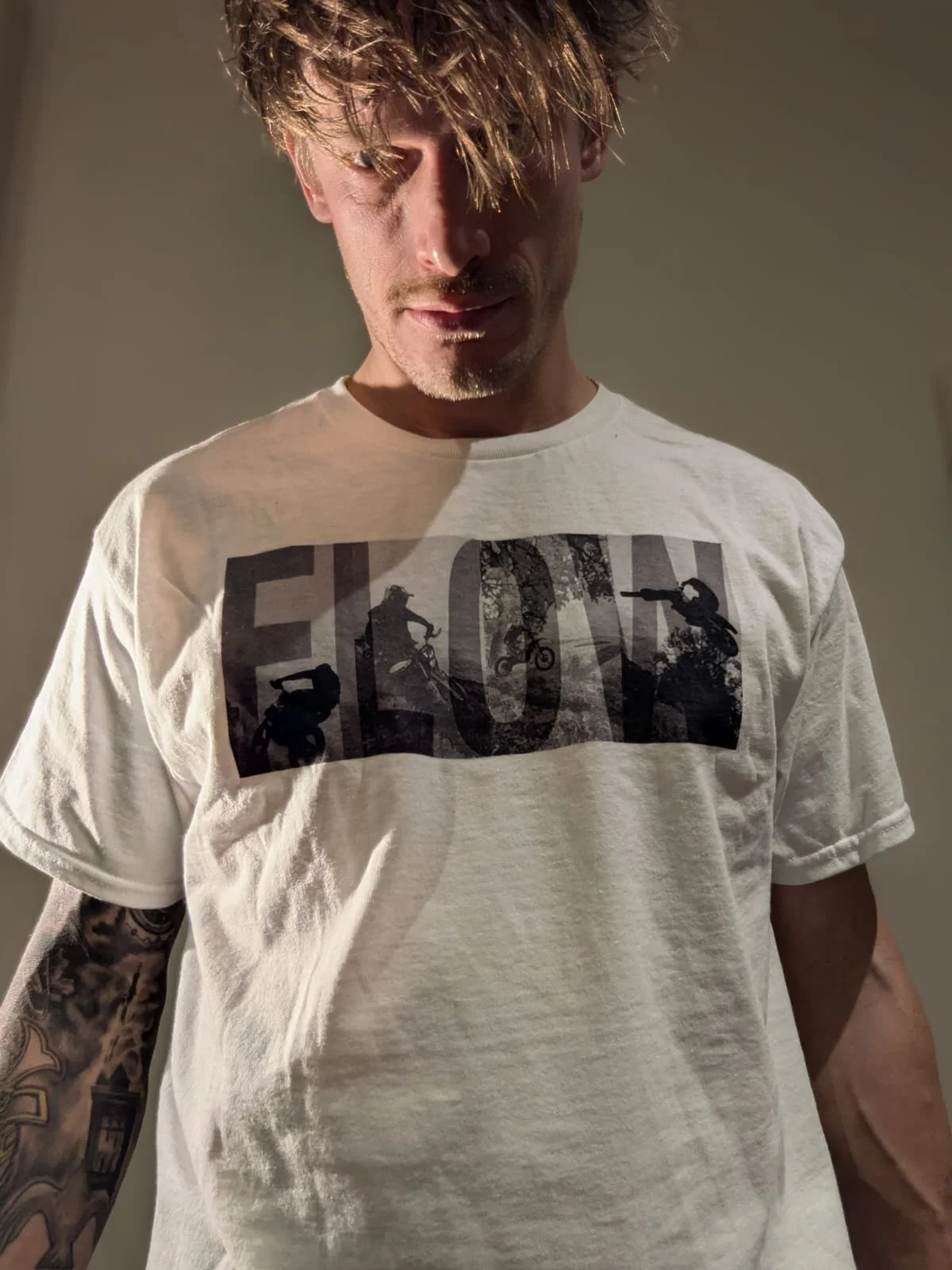 Model wearing dirt bike inspired graphic t shirt with the slogan 'flow' and dirt bike riders in the background