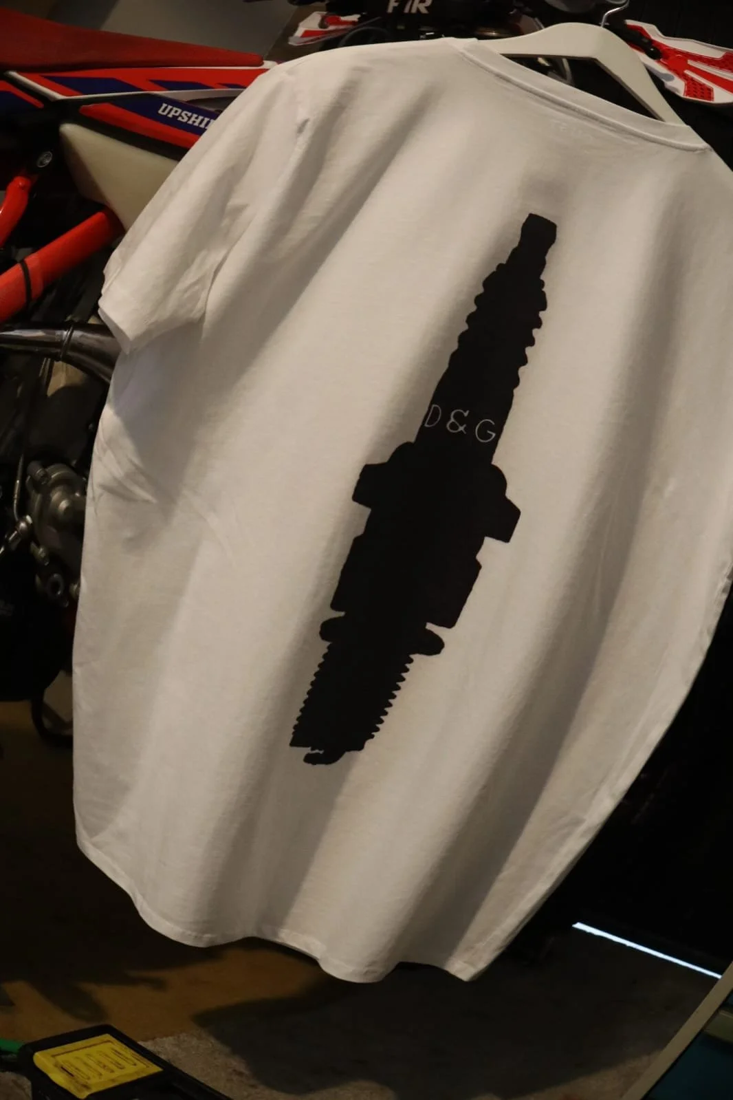 White spark plug t shirt hanging on enduro bike in the garage